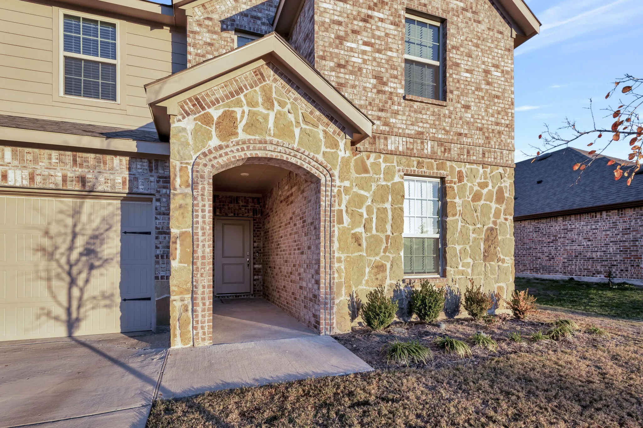 Stone and brick exterior with a covered entry, attached garage, and landscaping