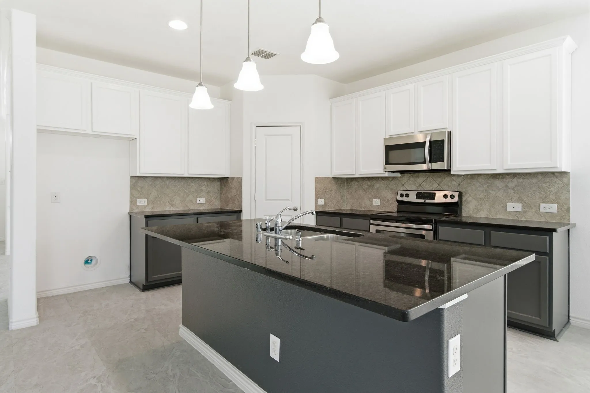 Kitchen featuring a central island with a sink, stainless steel appliances, white upper cabinetry, dark lower cabinetry, and a patterned backsplash
