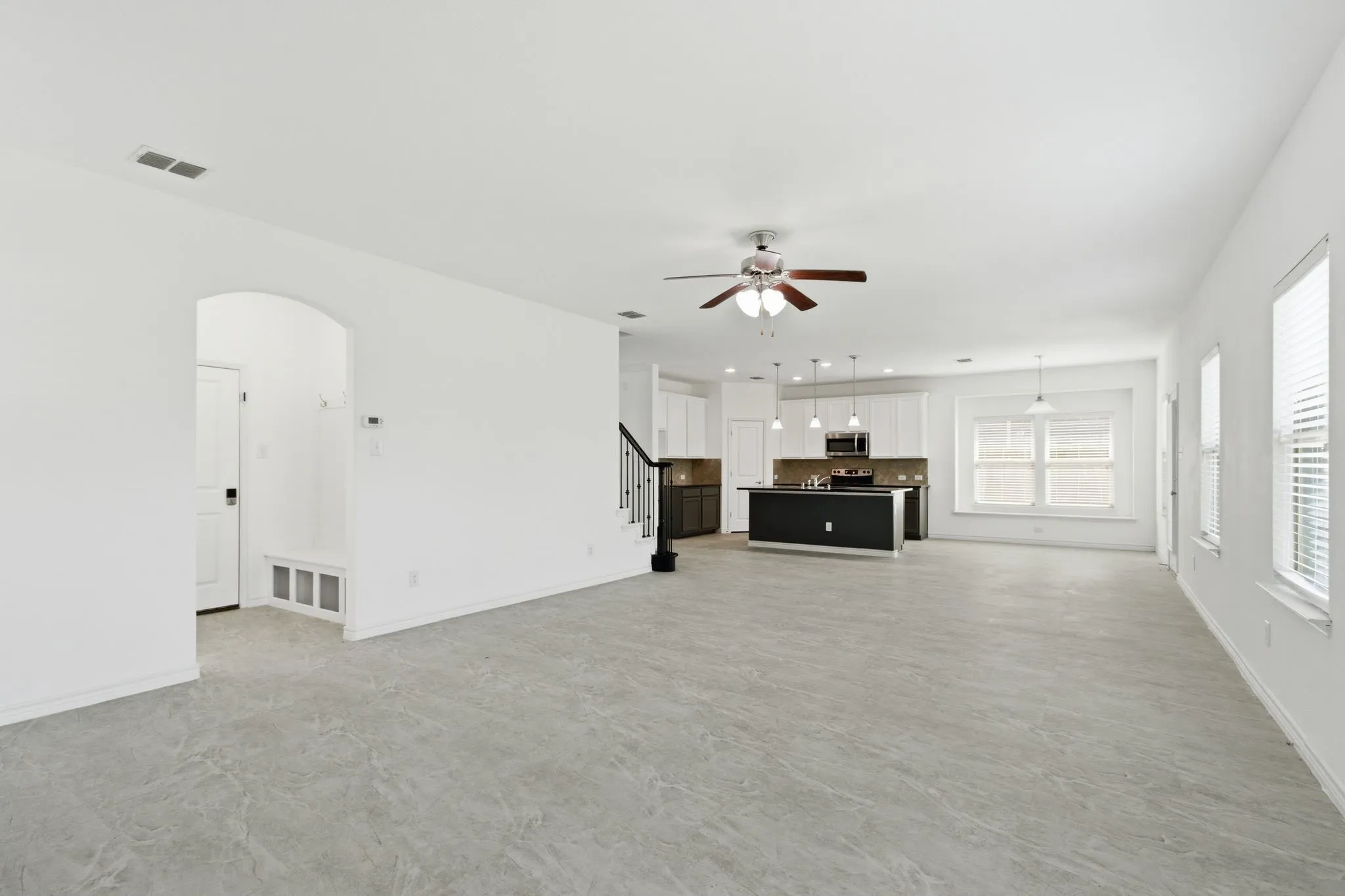 Open-concept living area with tile flooring, a ceiling fan, and multiple windows