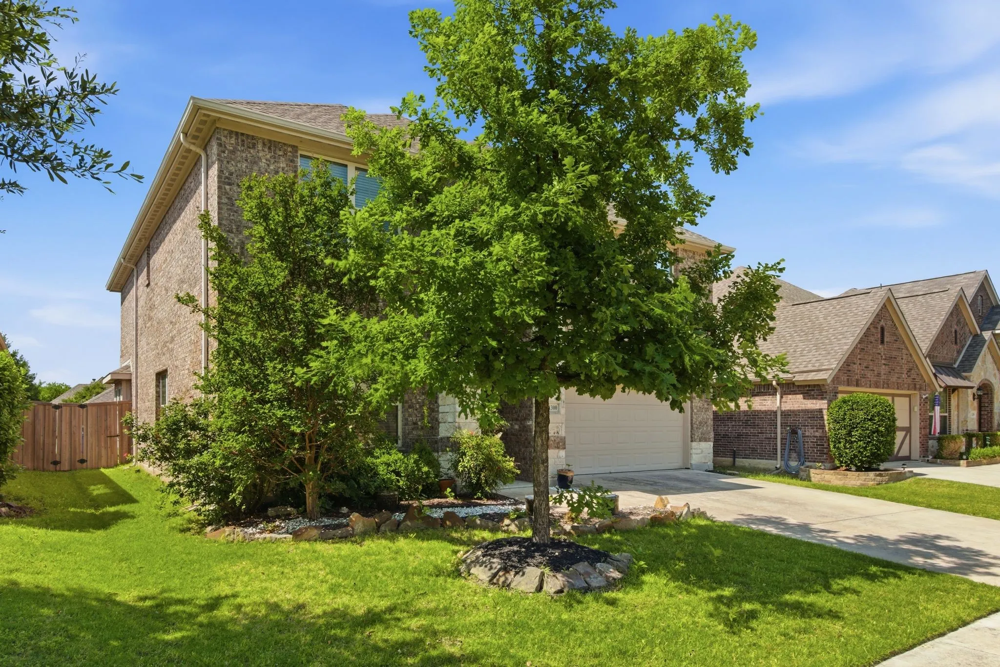 Brick exterior with stone accents, attached garage, concrete driveway, and a fenced side yard