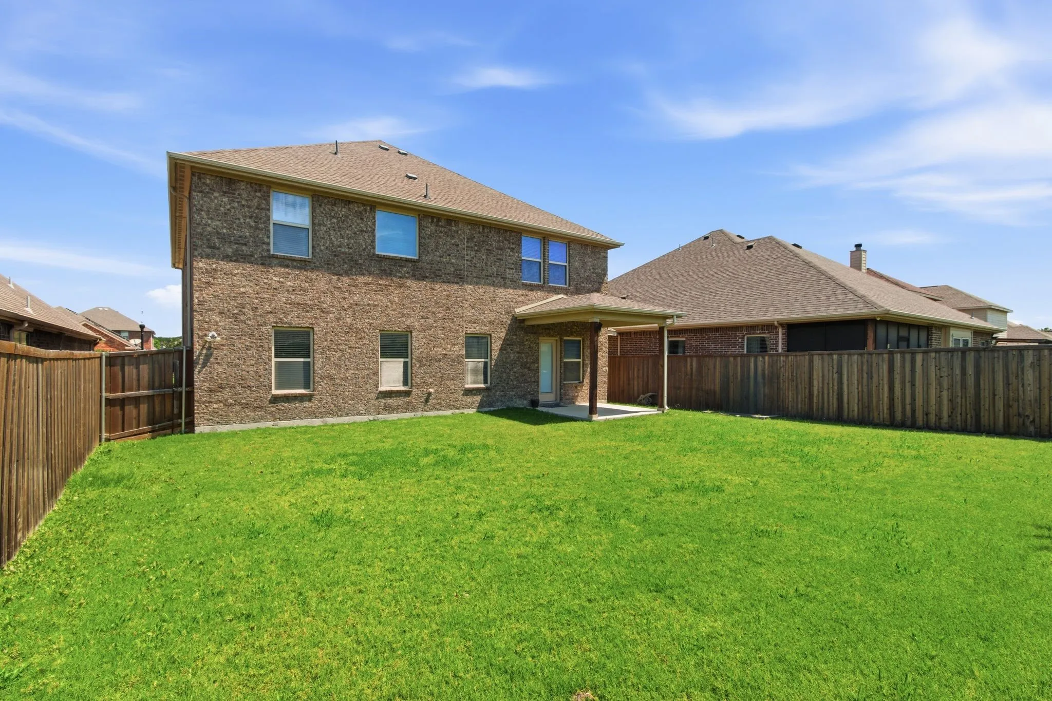 Expansive backyard featuring a manicured lawn, full privacy fencing, and a covered patio area