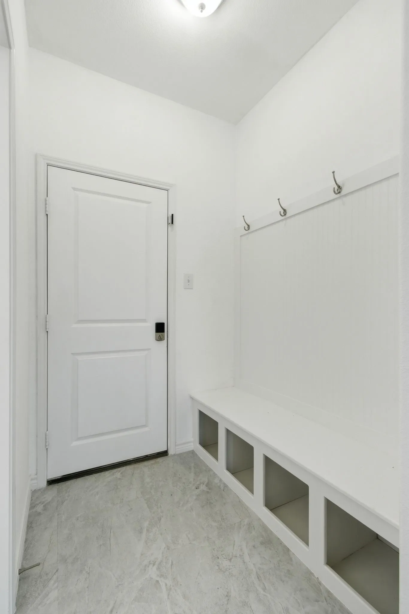 Built-in bench with storage cubbies, wall-mounted coat hooks, and light gray patterned flooring