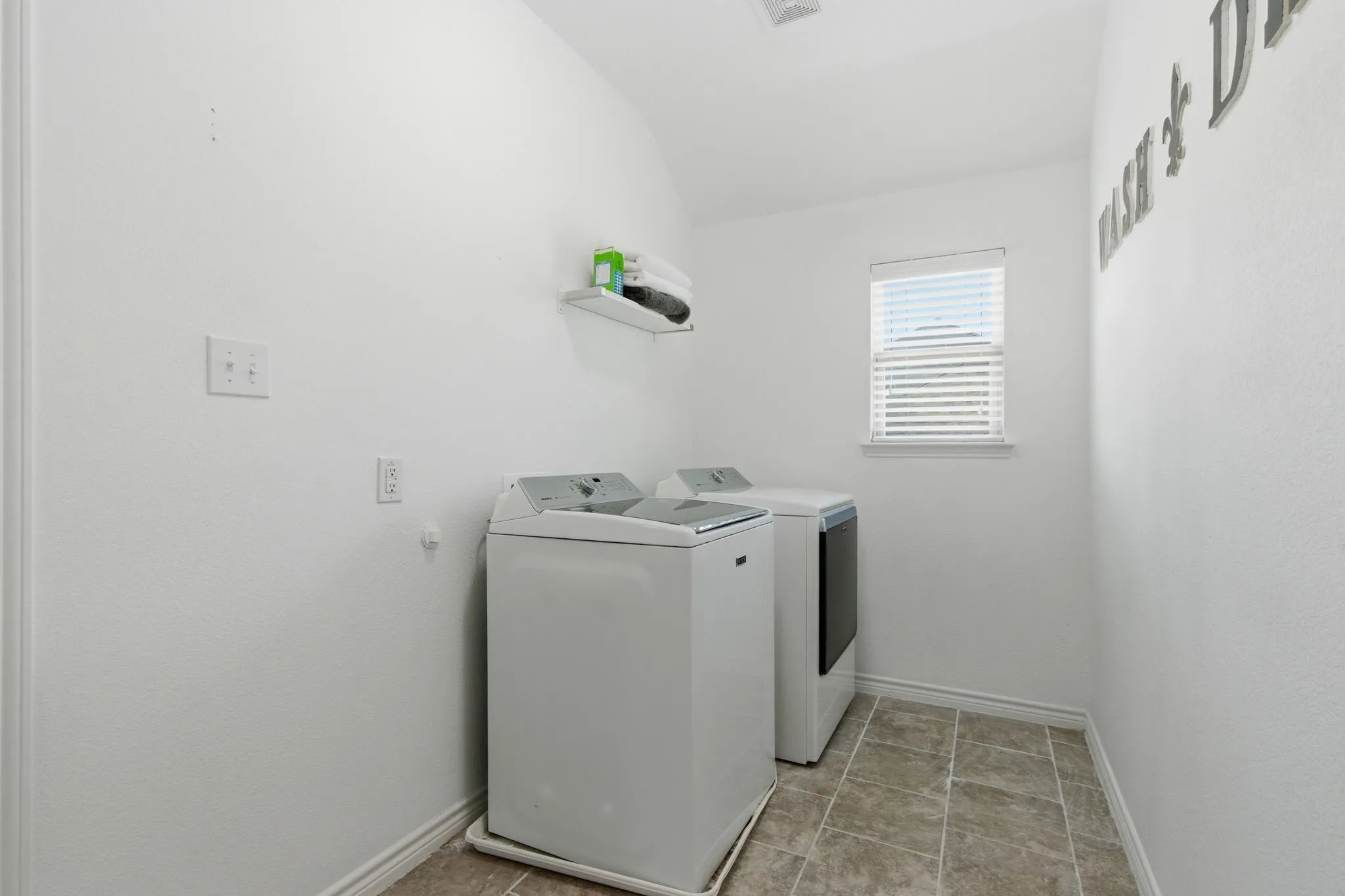 Laundry area featuring tile flooring, a window with blinds, and a wall-mounted shelf