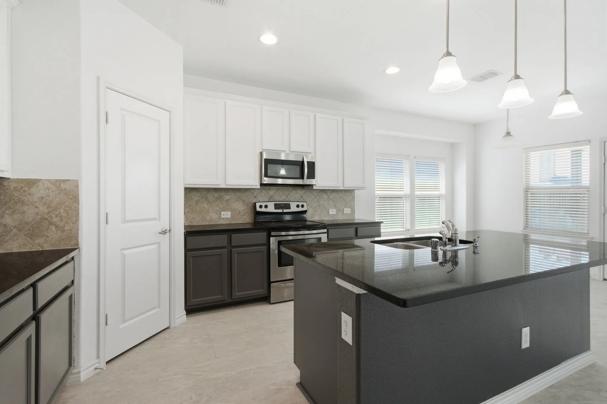 Kitchen with stainless steel appliances, dark countertops, white upper cabinetry, and a central island with an undermount sink