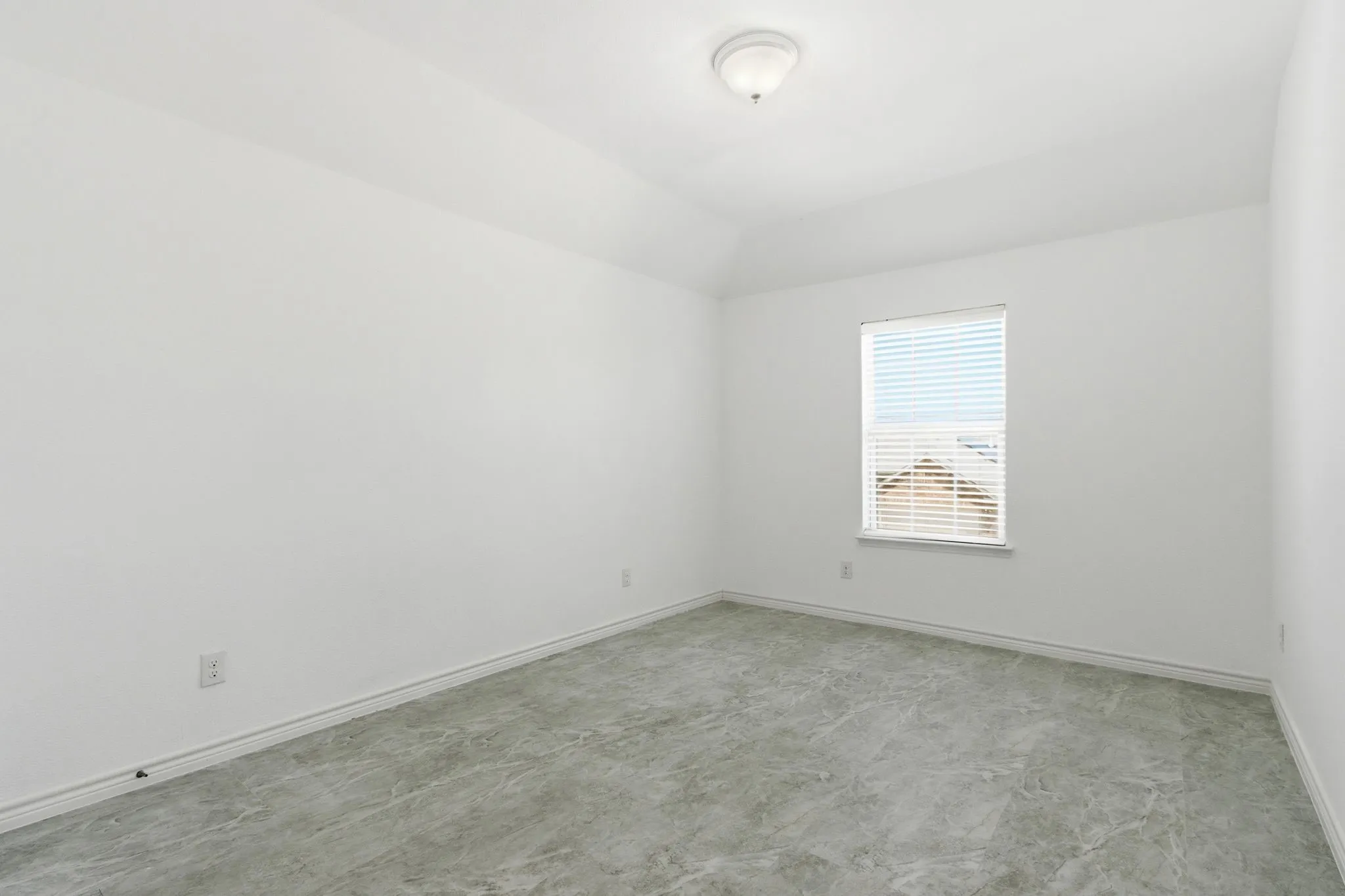 Bright bedroom featuring neutral wall finishes, large window with horizontal blinds providing natural light, and concrete flooring throughout