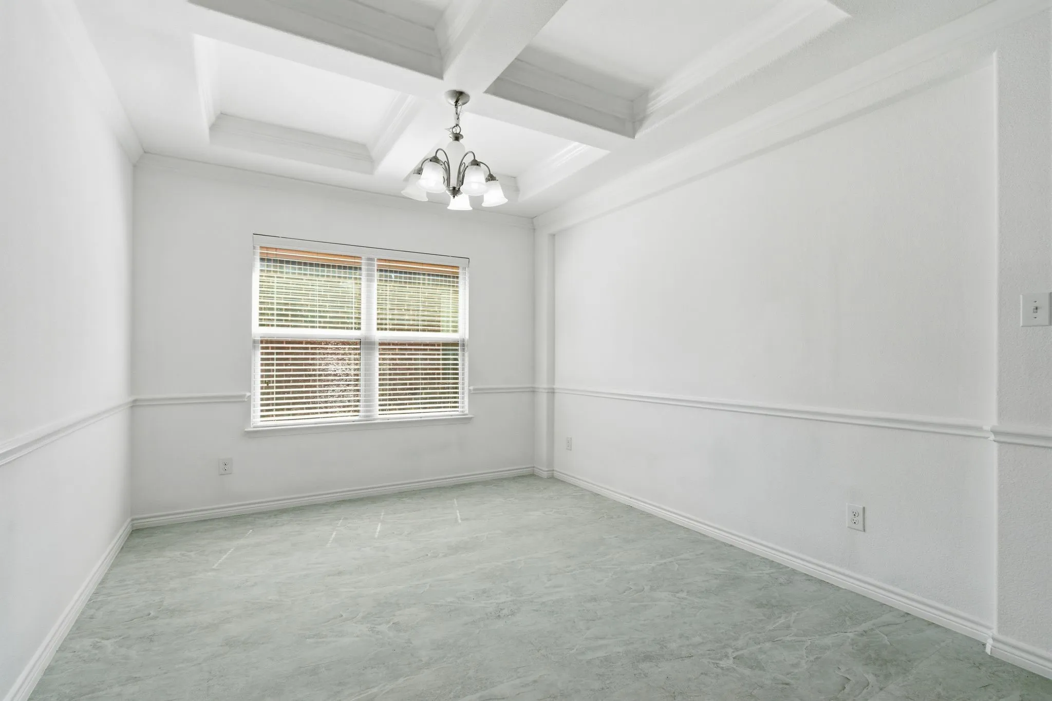 Tray ceiling with a decorative chandelier, white walls with chair rail molding, and a single window with blinds