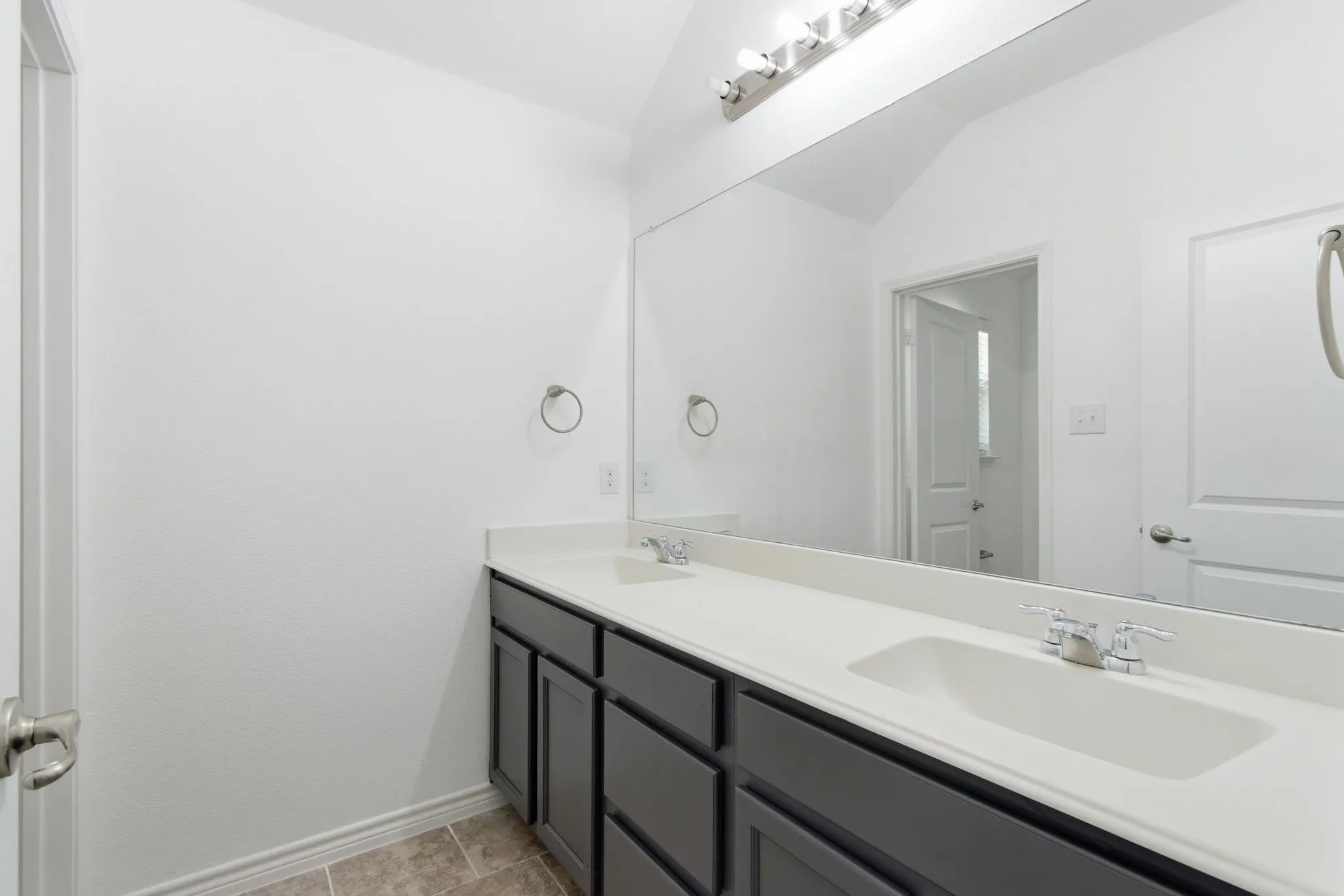 Dual vanity with dark wood-finish cabinetry, integrated sinks, chrome faucets, and an expansive wall-mounted mirror