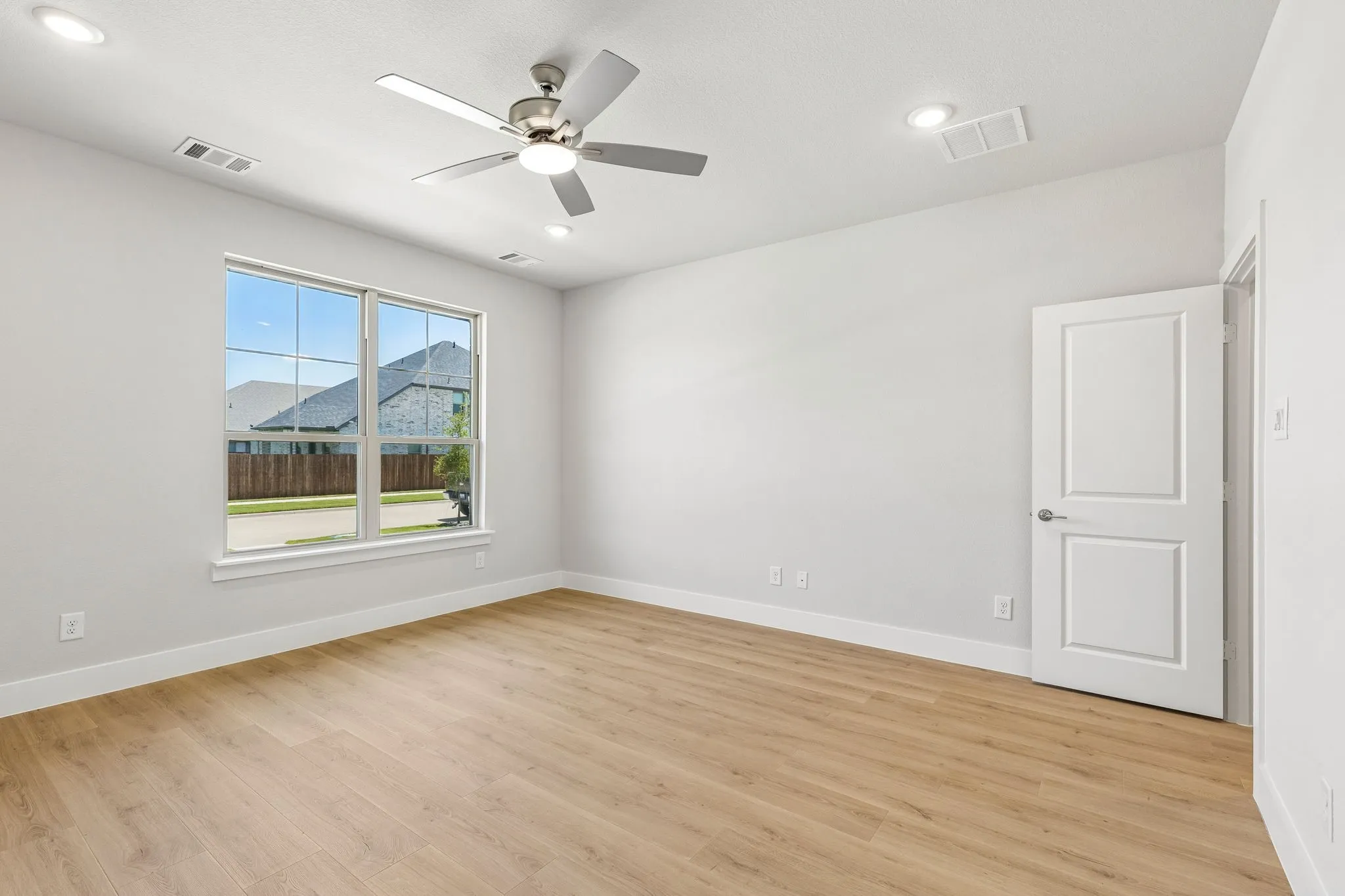 Light-filled room featuring wood-finish flooring, a ceiling fan, recessed lighting, and a paneled interior door with lever hardware