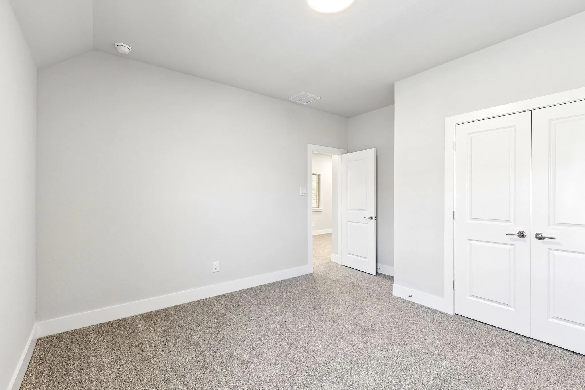 Neutral-toned carpeting with white baseboards, a flush-mount ceiling light, and white paneled doors with satin nickel hardware