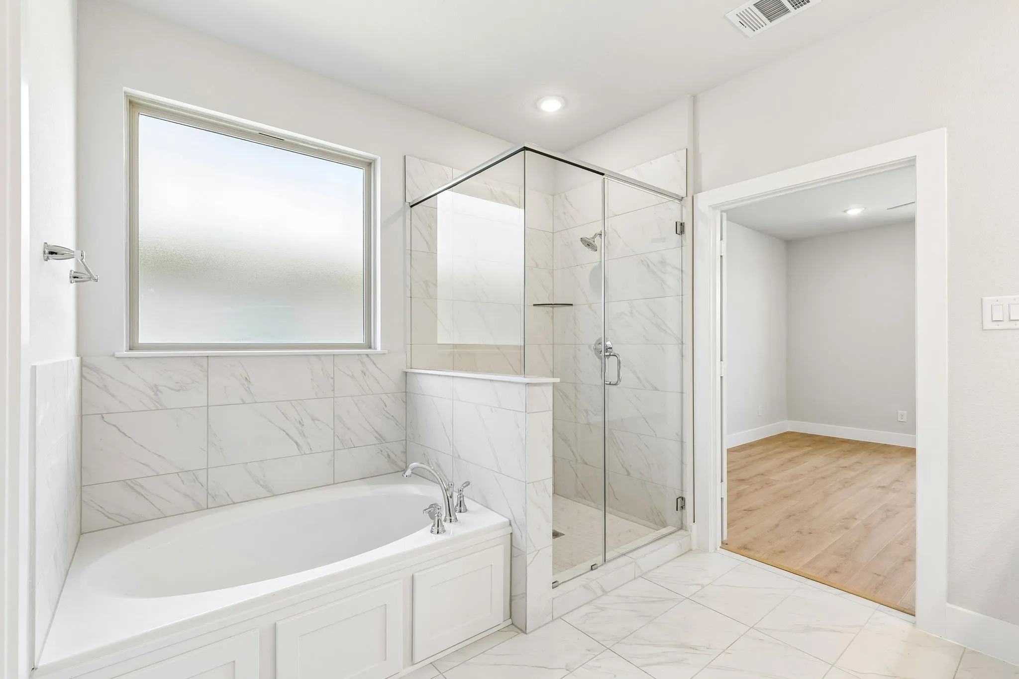Recessed soaking tub with paneling, enclosed glass shower, frosted window, and white tile flooring