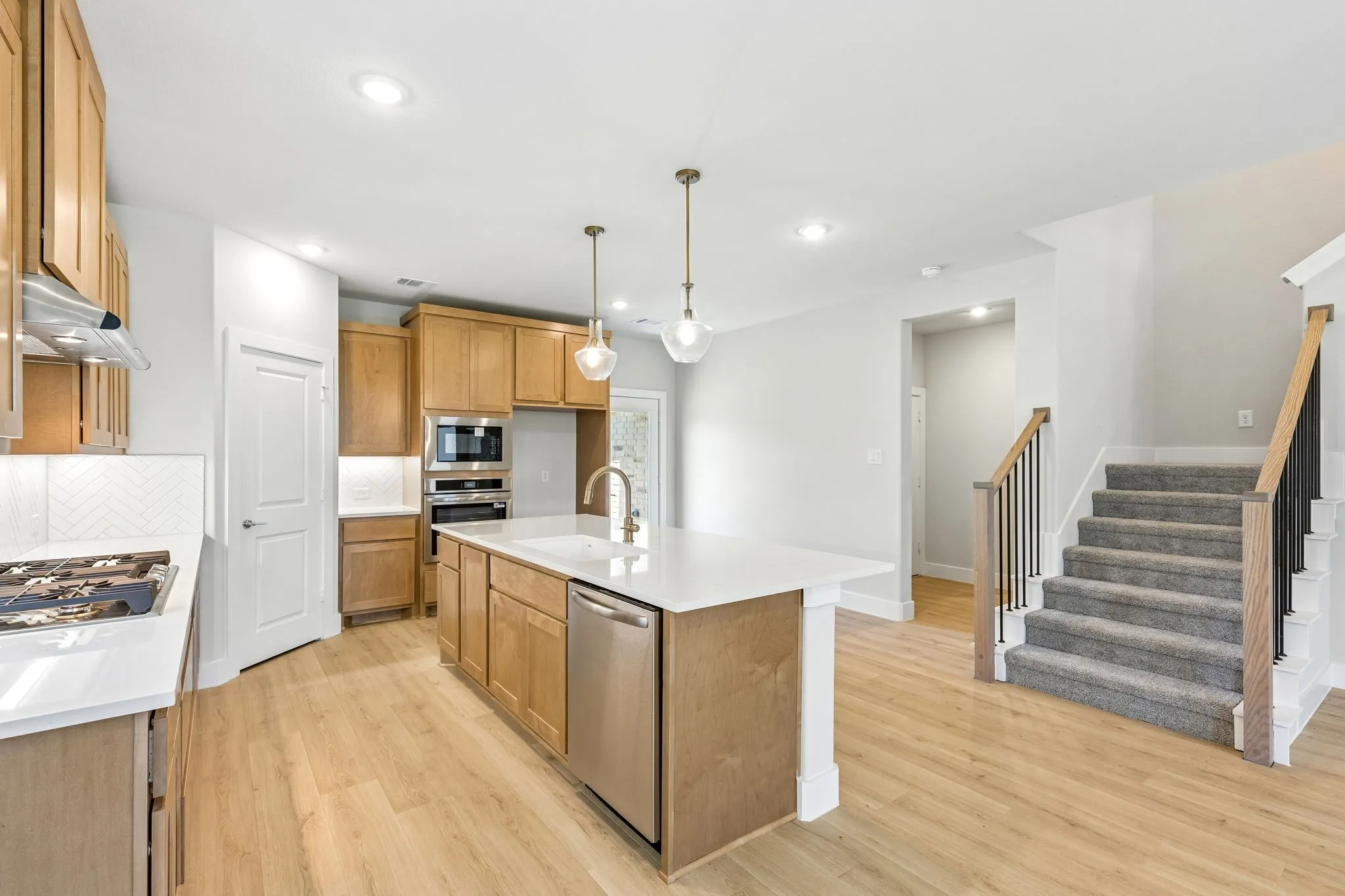 Kitchen featuring light wood-finish cabinetry, stainless steel appliances, a center island with sink, and solid surface countertops