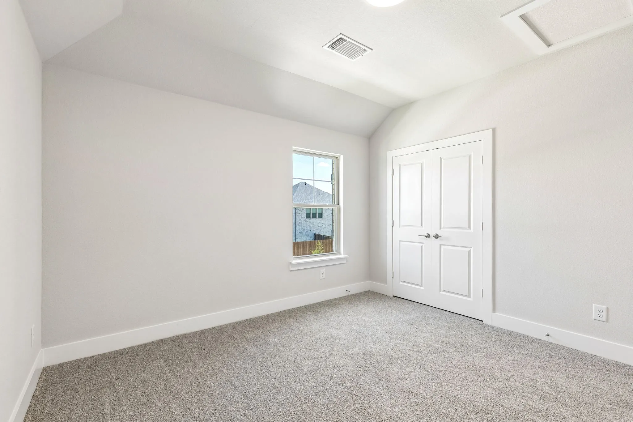 Vaulted ceiling, neutral wall tones, window with white trim, double panel doors, and gray carpeting