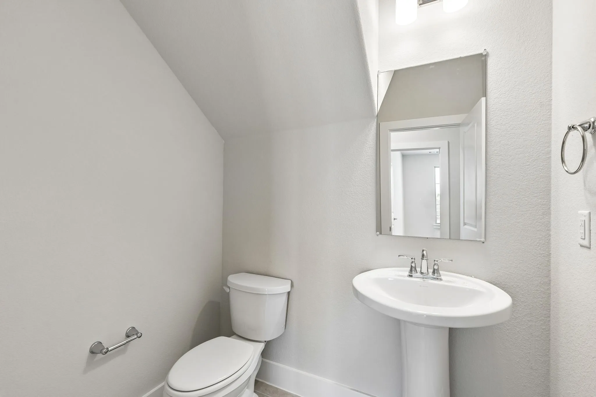 Pedestal sink with chrome faucet, mirror, wall-mounted light fixture, and toilet