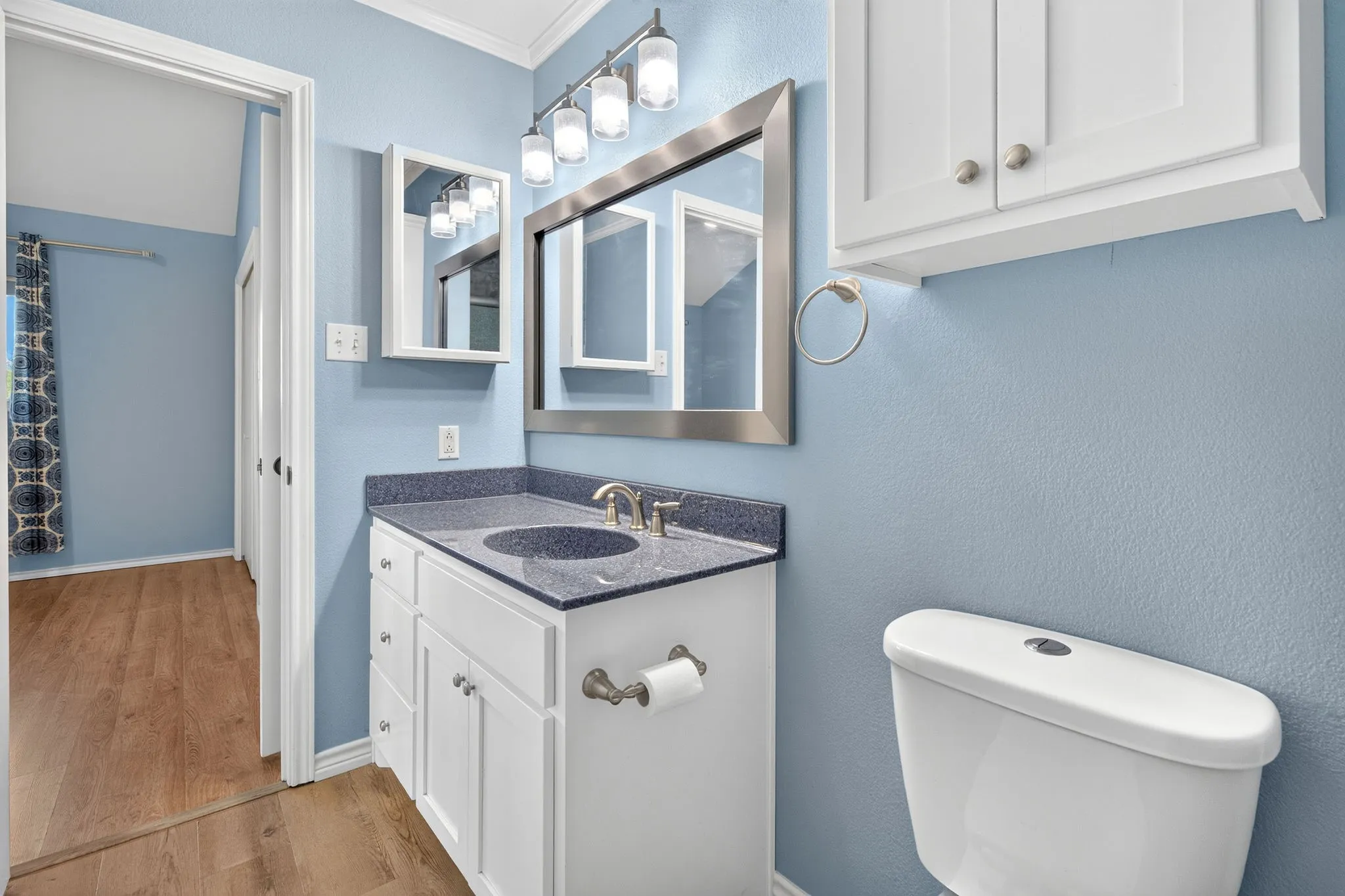 White vanity cabinet with dark speckled countertop and sink, updated fixtures.