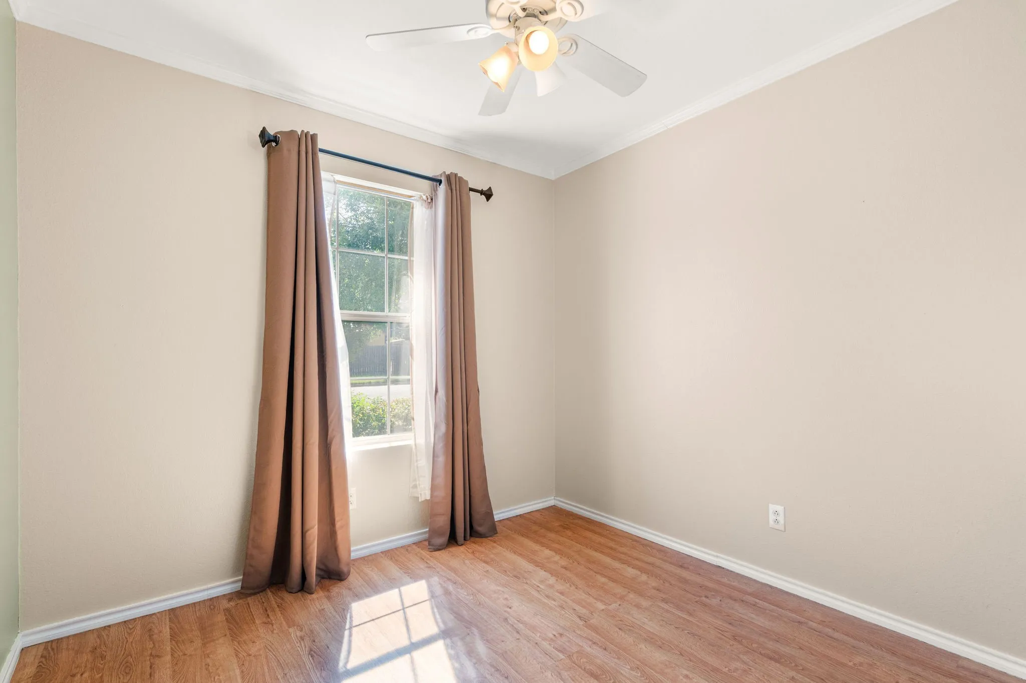 Wood-finish vinyl flooring, light-toned walls, and a ceiling fan with integrated lighting.  Window overlooks front yard.