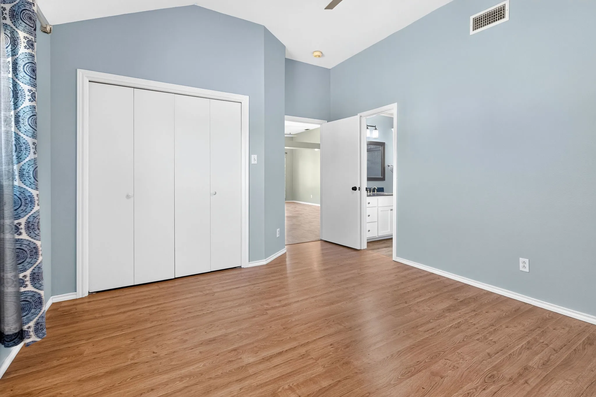 Wood-finish LVP flooring, vaulted ceiling, bi-fold closet doors, and light blue wall tones.  Entry to primary bath.