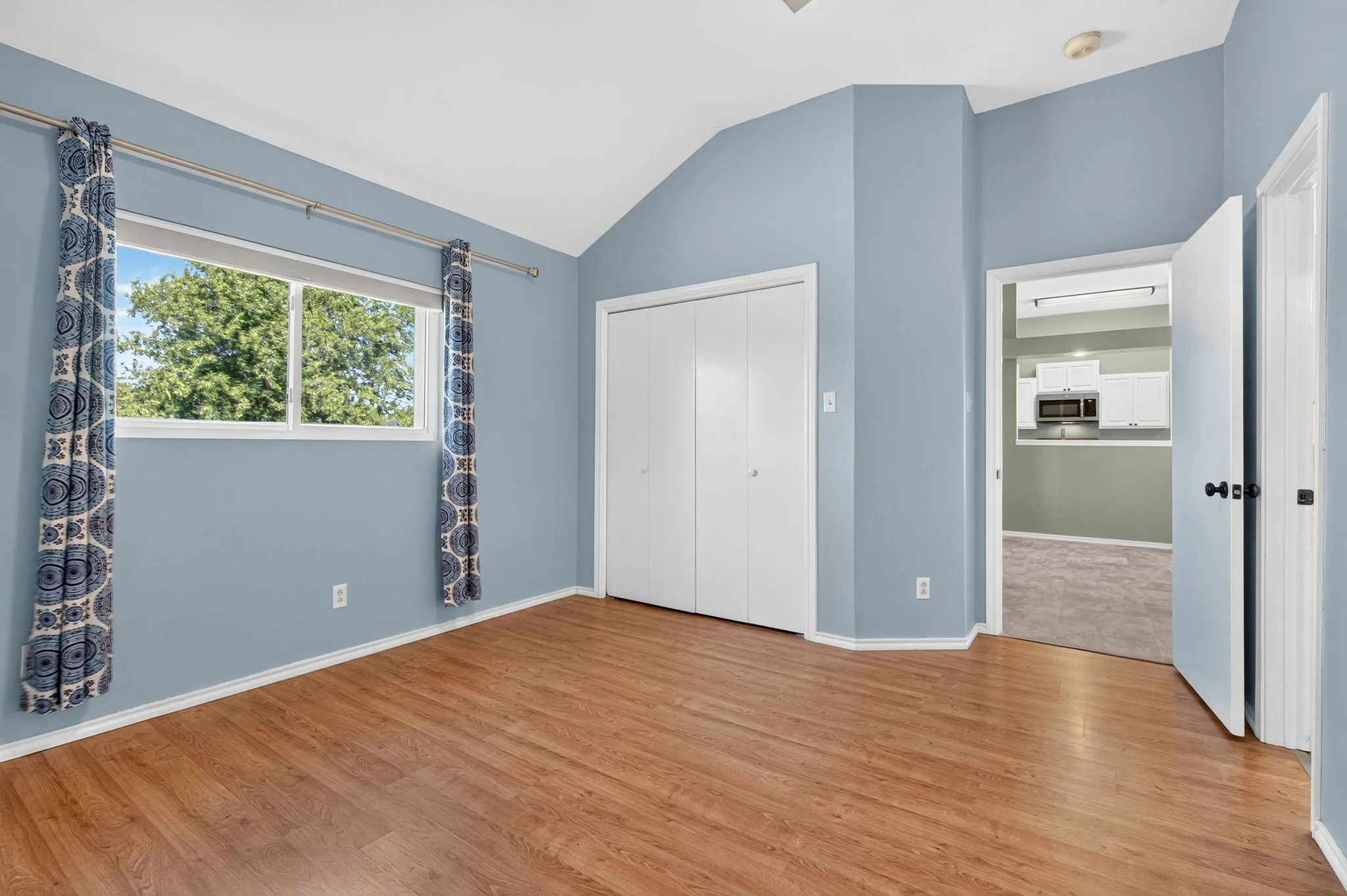 Wood-finish LVP flooring with a multi-pane window, vaulted ceiling, and bi-fold closet doors.
