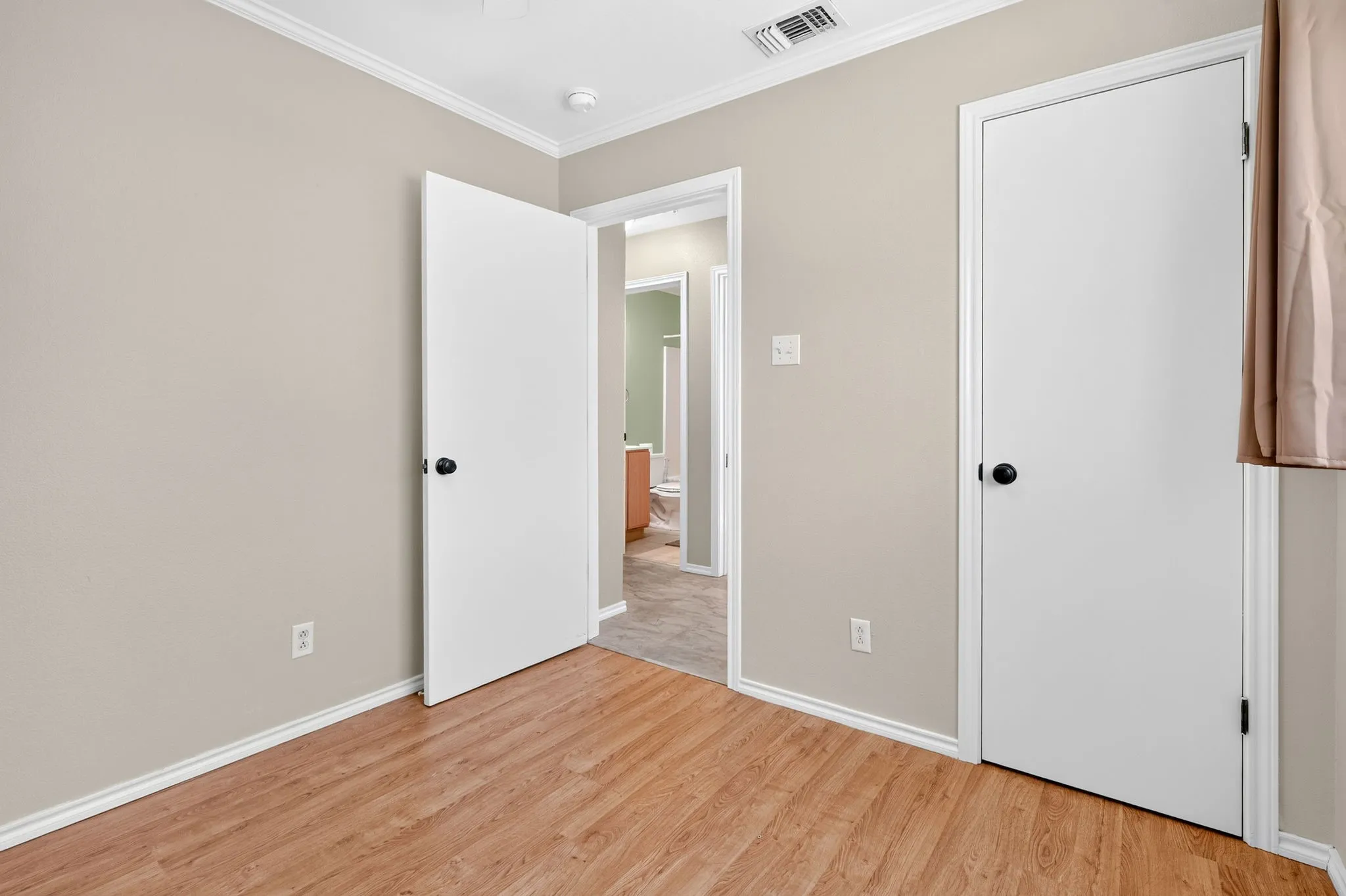 Wood-finish plank flooring with white baseboards, light neutral wall paint, and white crown molding