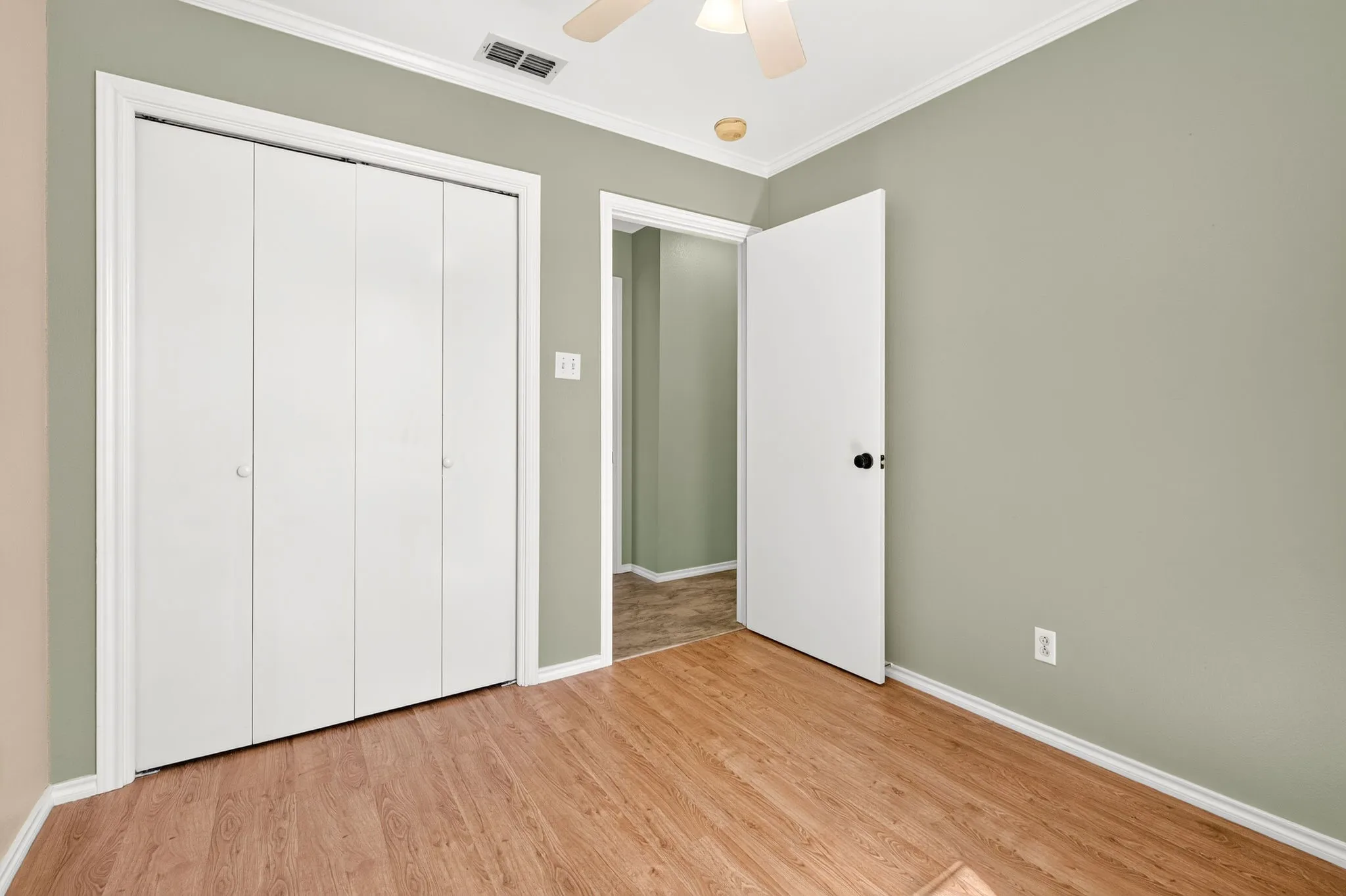 Wood-finish plank flooring, bi-fold closet doors, and ceiling fan in front bedroom.