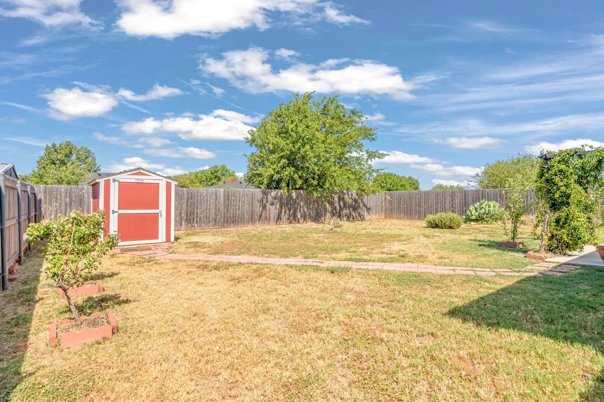Backyard featuring a wood fence, red storage shed, and a pave stone pathway.