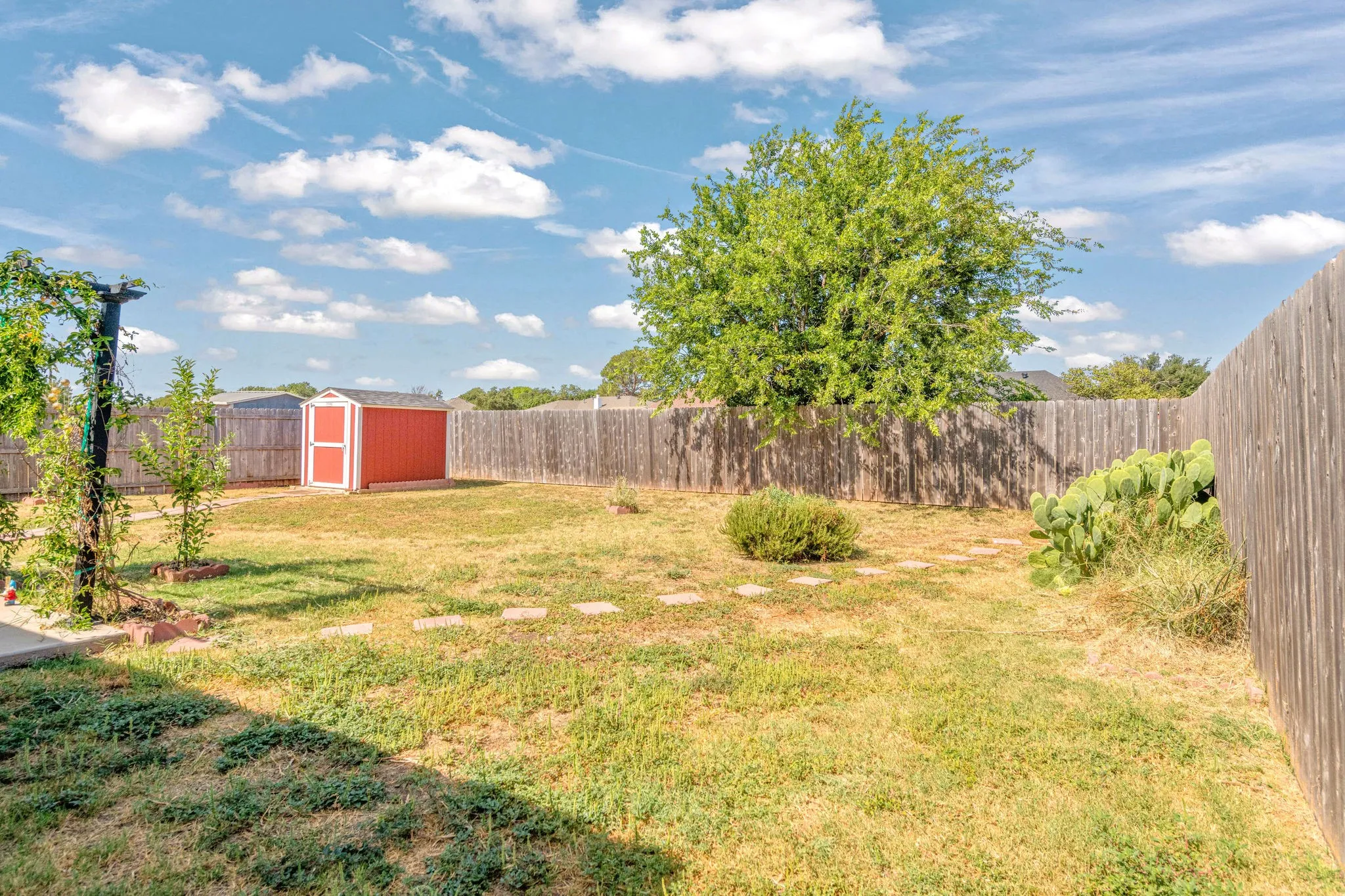 Expansive fenced yard with a red storage shed, established trees, and stepping stones.