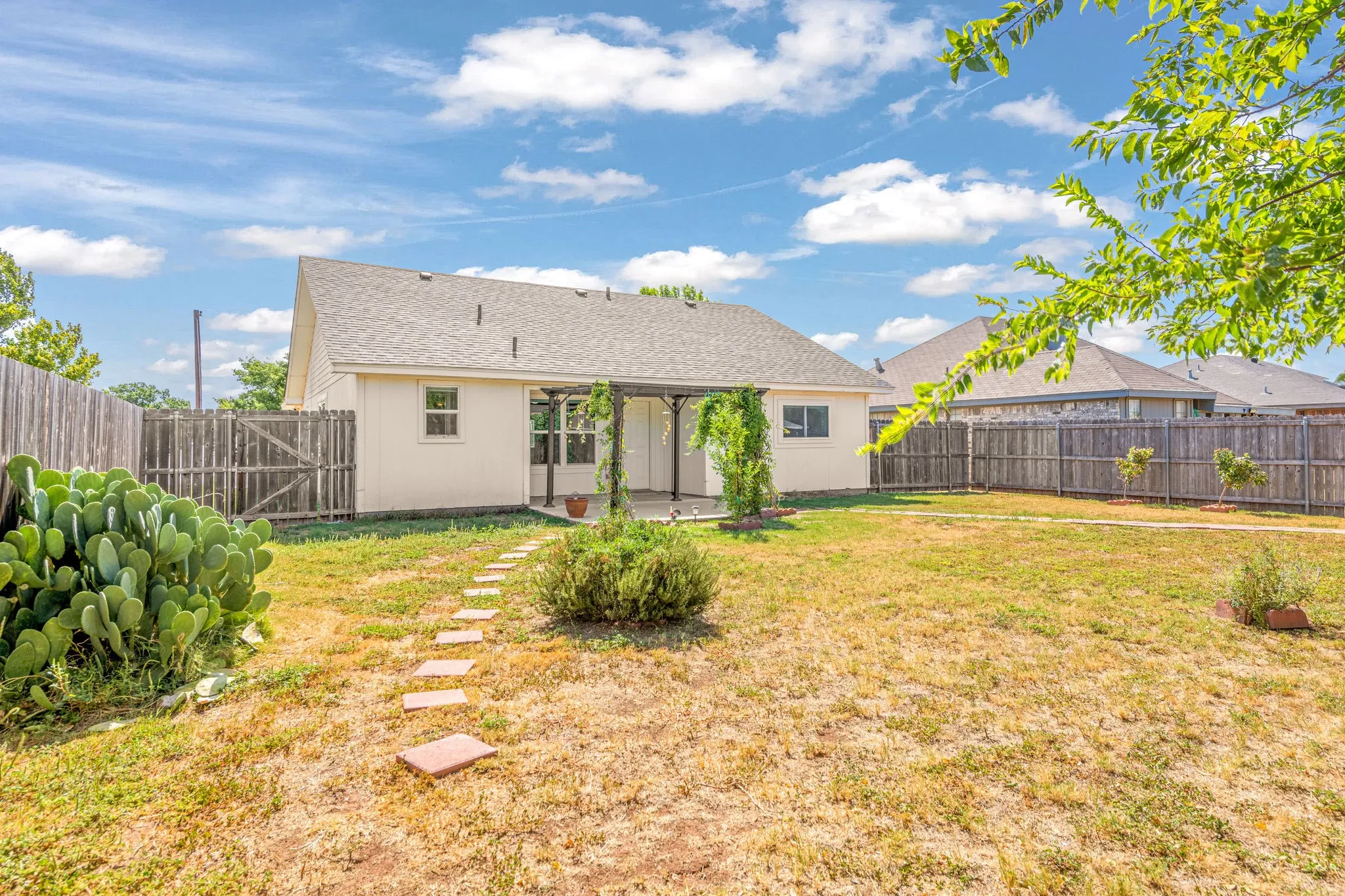Backyard featuring a privacy fence, stone paver pathways, covered patio, and mature landscaping.