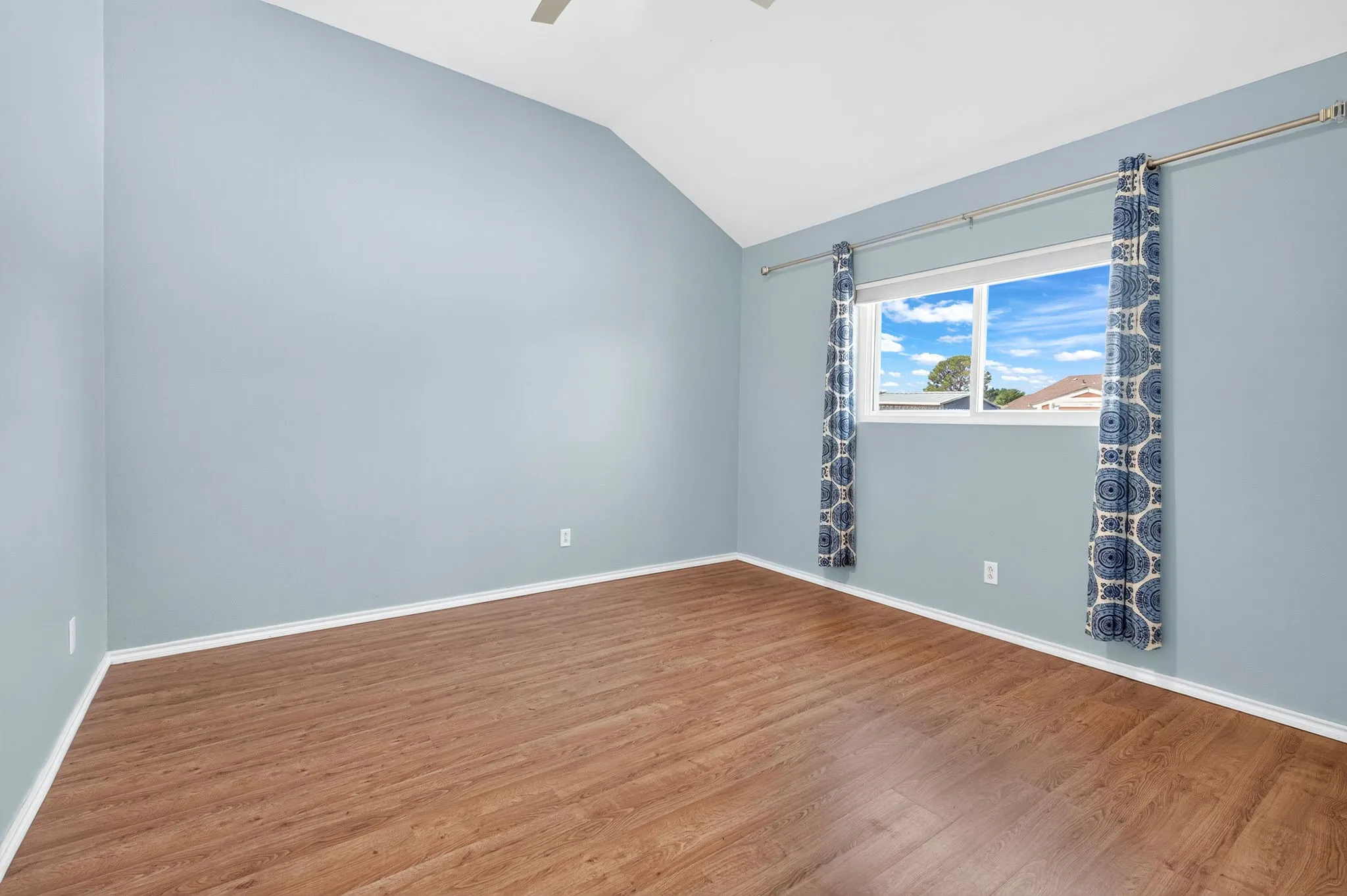 Vaulted ceiling with a ceiling fan, wood-finish LVP flooring, and a large window overlooking back yard.