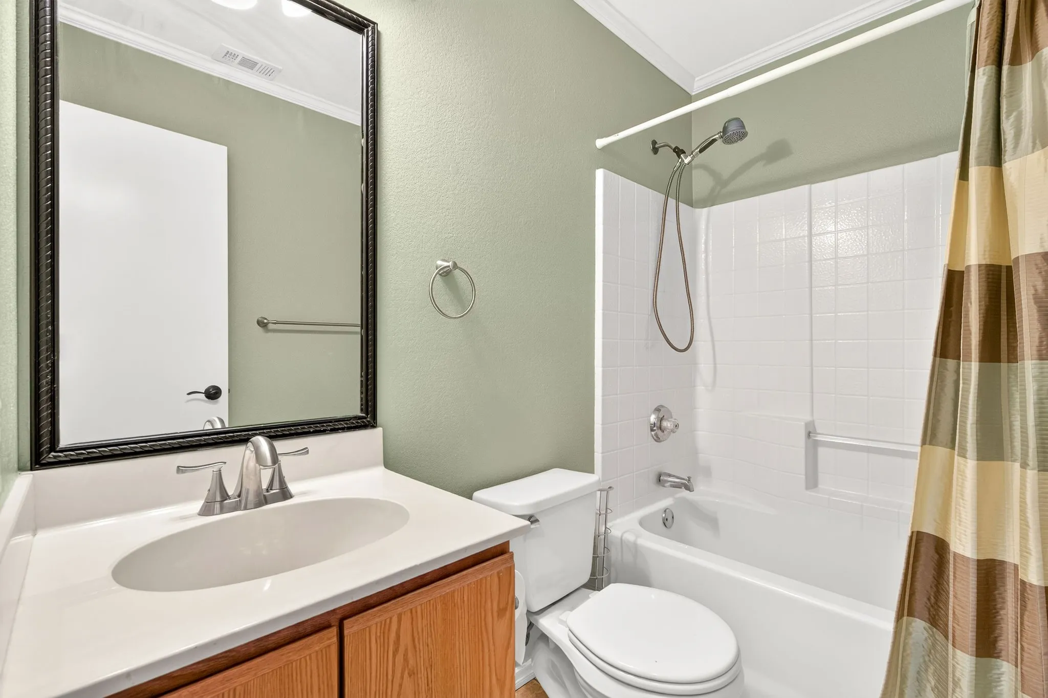 Wood-finish vanity with a white countertop and oval sink, brushed nickel faucet, and a large framed​​‌​​​​‌​​‌‌​‌‌​​​‌‌​‌​‌​‌​​​‌​​ mirror.