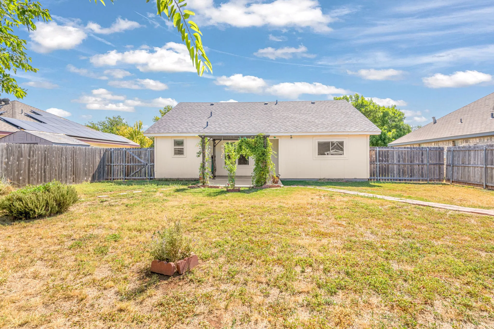 Backyard featuring a covered back patio with a metal pergola, surrounded by a wood fence.