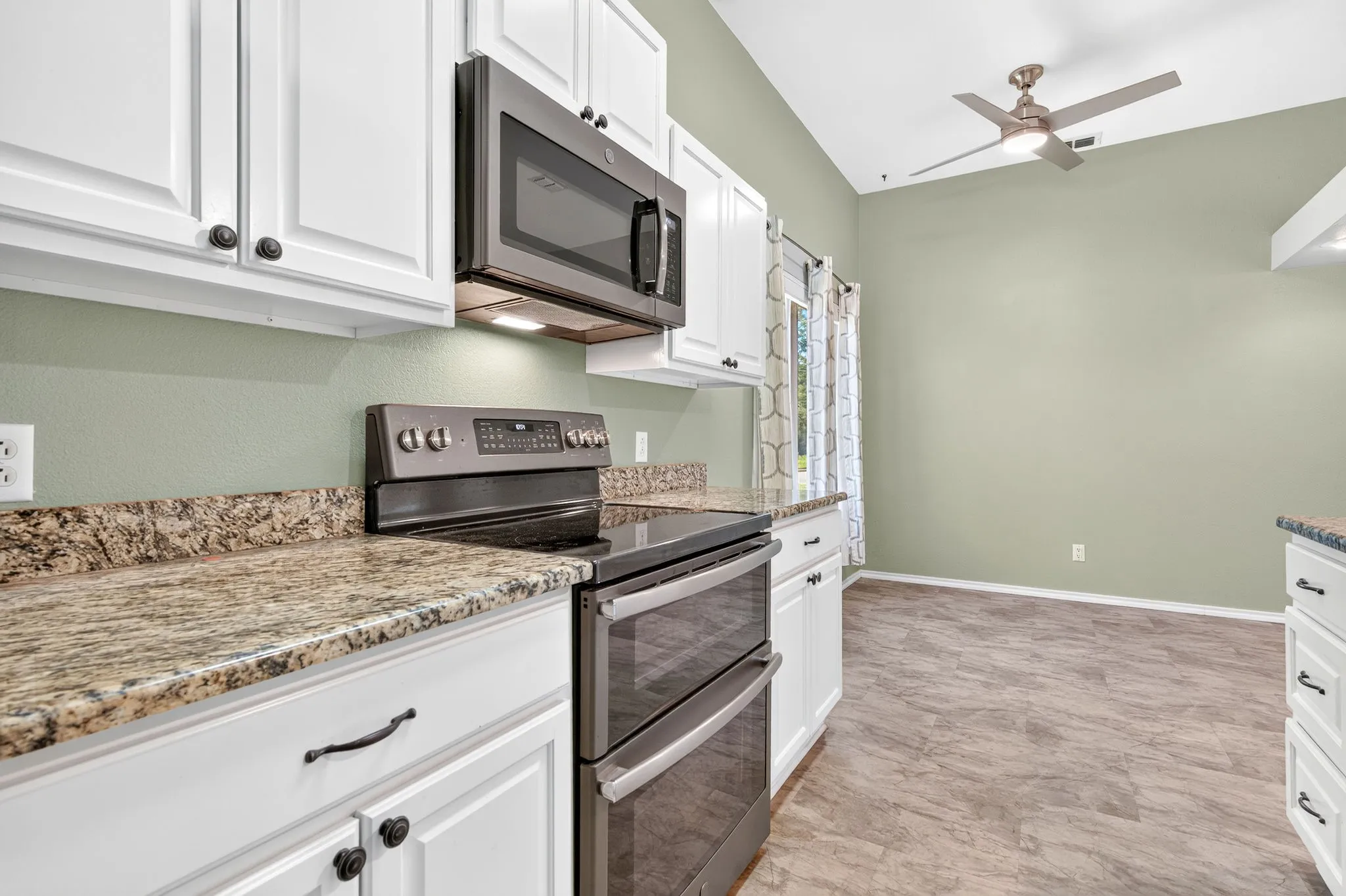 White cabinetry with dark hardware, granite countertops, stainless steel appliances, and a ceiling fan in dining area.