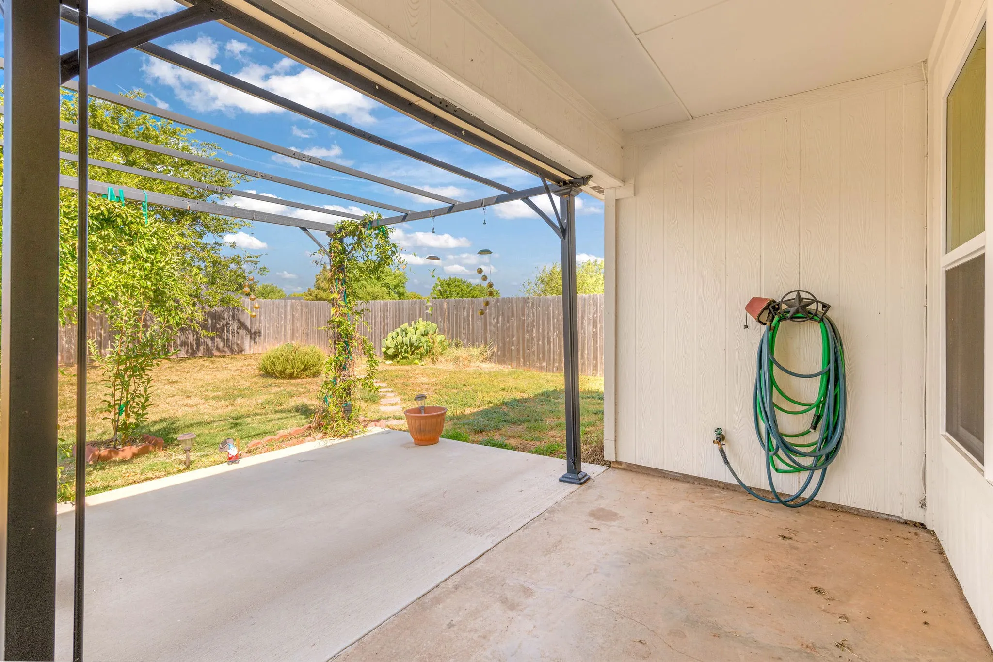 Covered back patio with a metal pergola structure, concrete extended patio, and a fully fenced backyard.