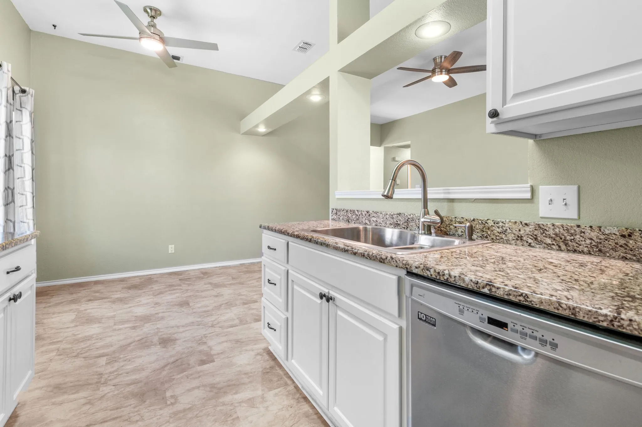 Granite countertops, stainless steel sink with a high-arch faucet, white cabinetry, dishwasher, and  high ceilings with ceiling fans.