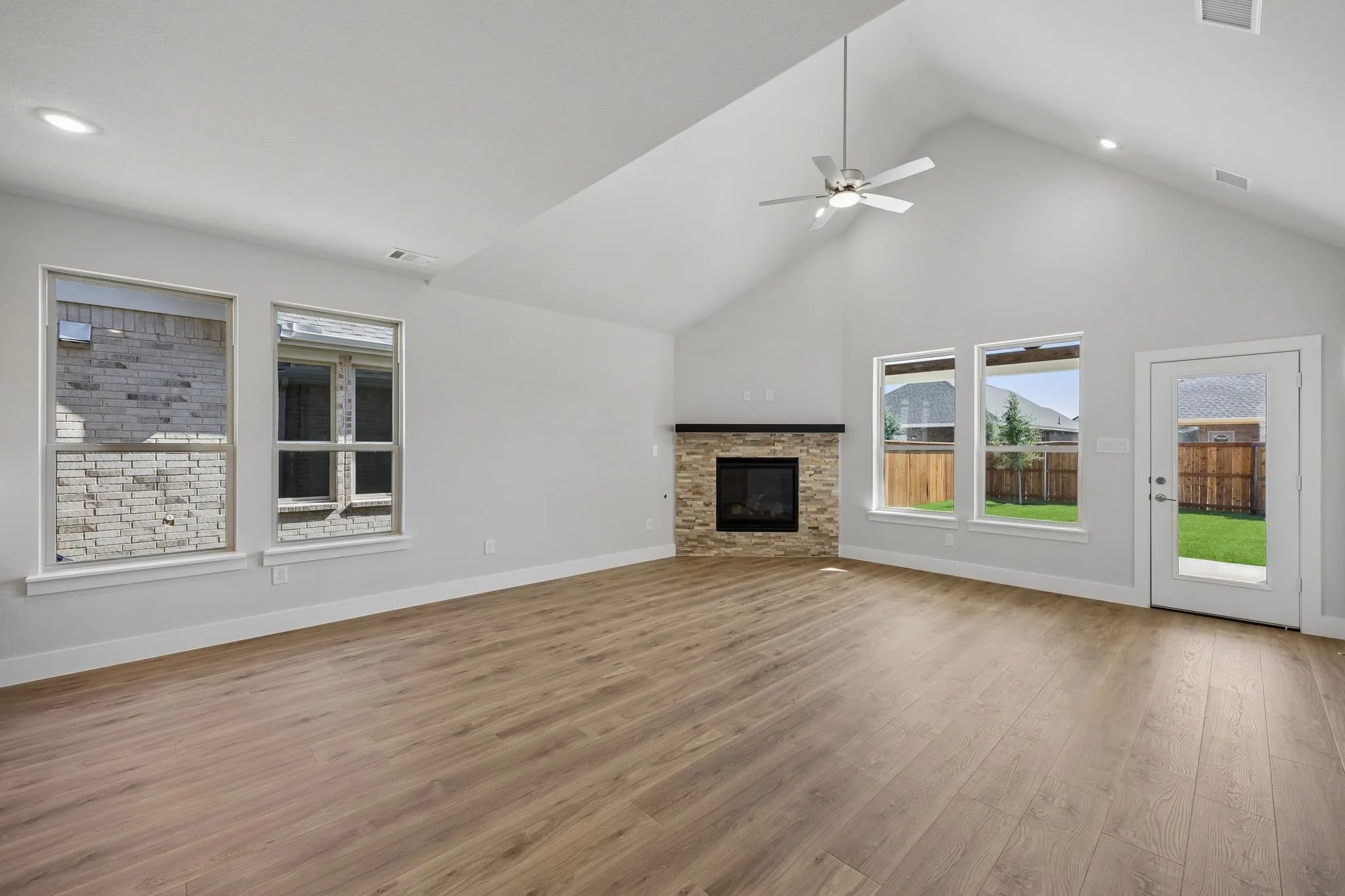 Vaulted ceiling with recessed lighting, wood-finish flooring, stone-clad fireplace, ceiling fan, and backyard access