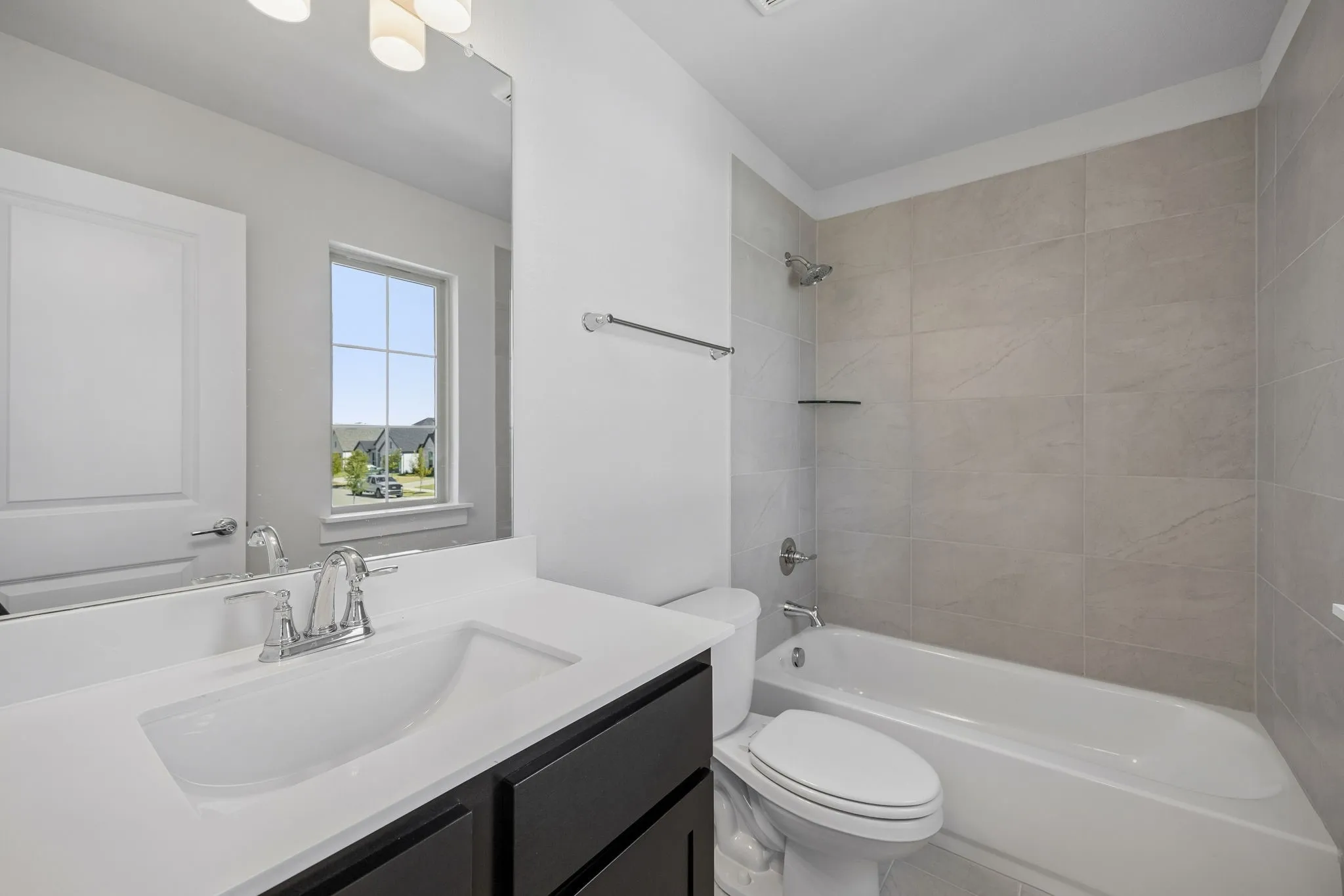Contemporary bathroom featuring a single vanity with a white countertop and dark cabinetry, a chrome faucet, a large wall-mounted mirror, and a tub with tiled surround