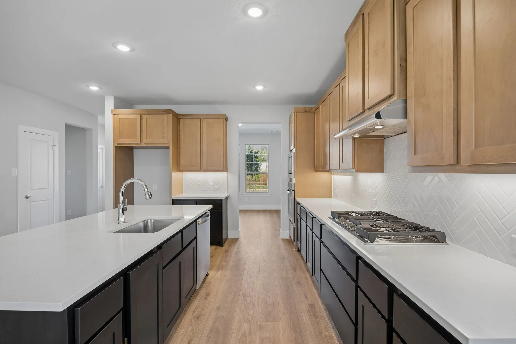 Kitchen featuring light wood-finish upper cabinetry, dark wood-finish lower cabinetry, white countertops, a gas cooktop, and a stainless steel sink