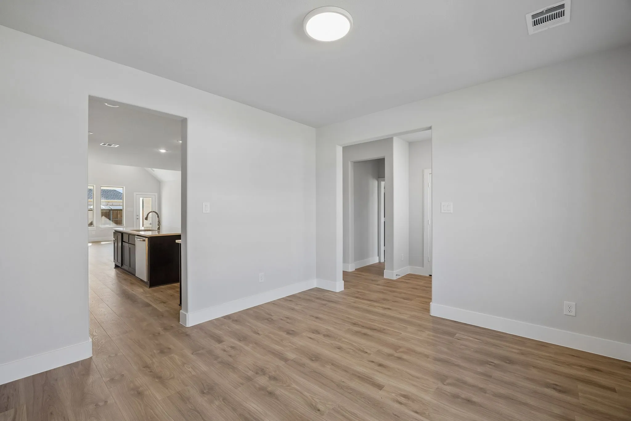 Recessed circular ceiling light, light wood-finish flooring, white wall paint, white trim, open doorways