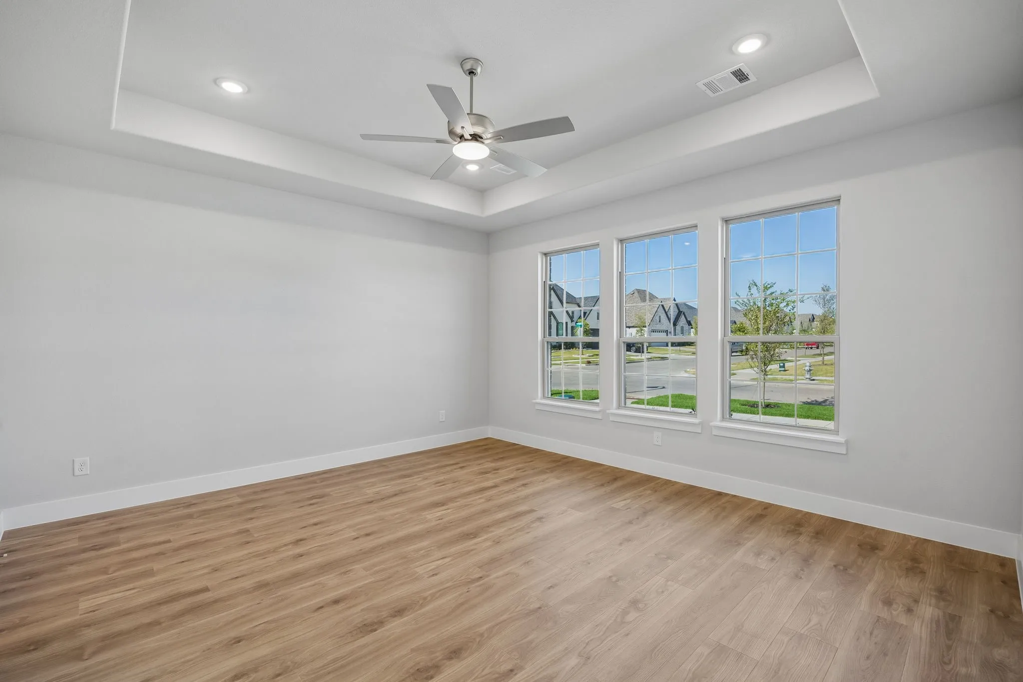 Tray ceiling with recessed lighting, ceiling fan, wood-finish flooring, and three large windows