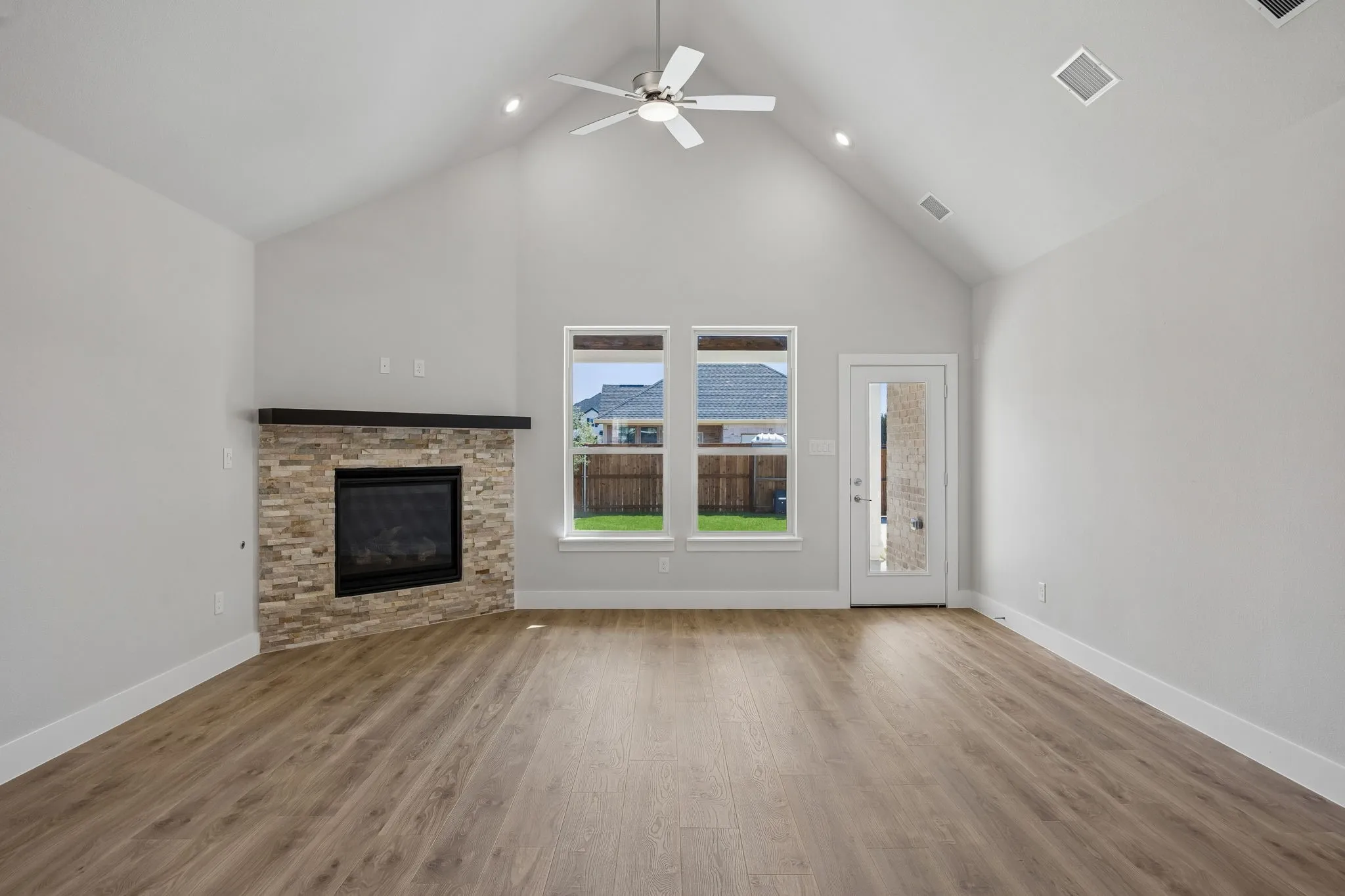 Vaulted ceiling with a ceiling fan and recessed lighting, wood-finish flooring, stone-clad fireplace with a dark wood mantel, and a glass-paned door