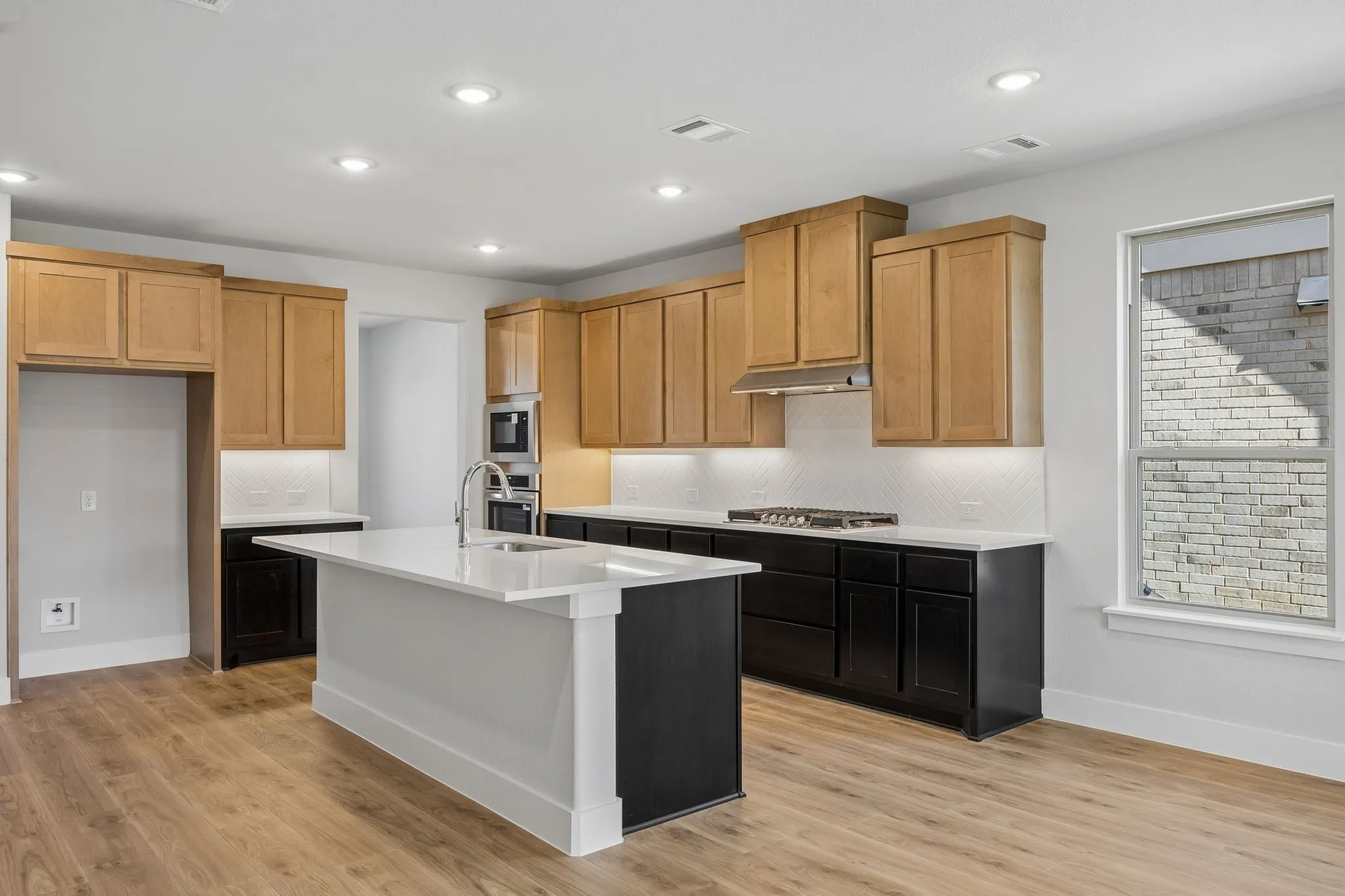 Kitchen featuring wood-finish flooring, recessed lighting, a kitchen island with sink, black base cabinetry, and natural wood upper cabinetry