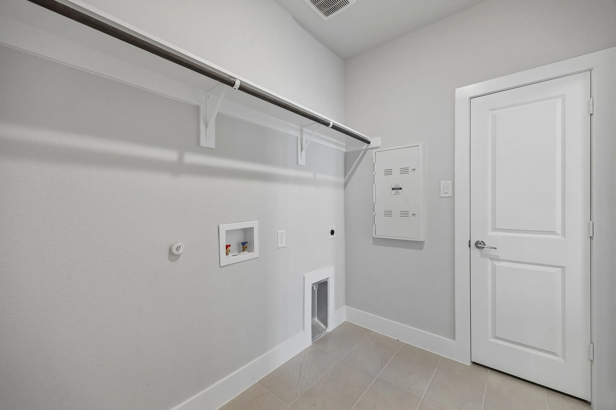 Laundry area with a hanging rod, utility connections, and light-toned tile flooring