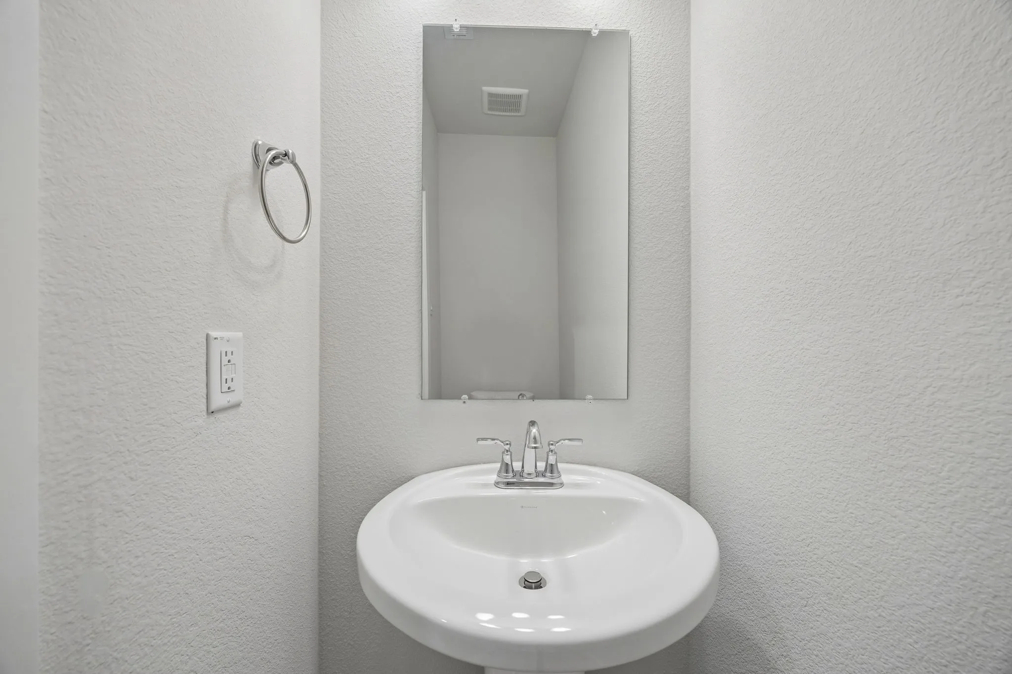 Pedestal sink with chrome faucet, wall-mounted mirror, and white textured walls