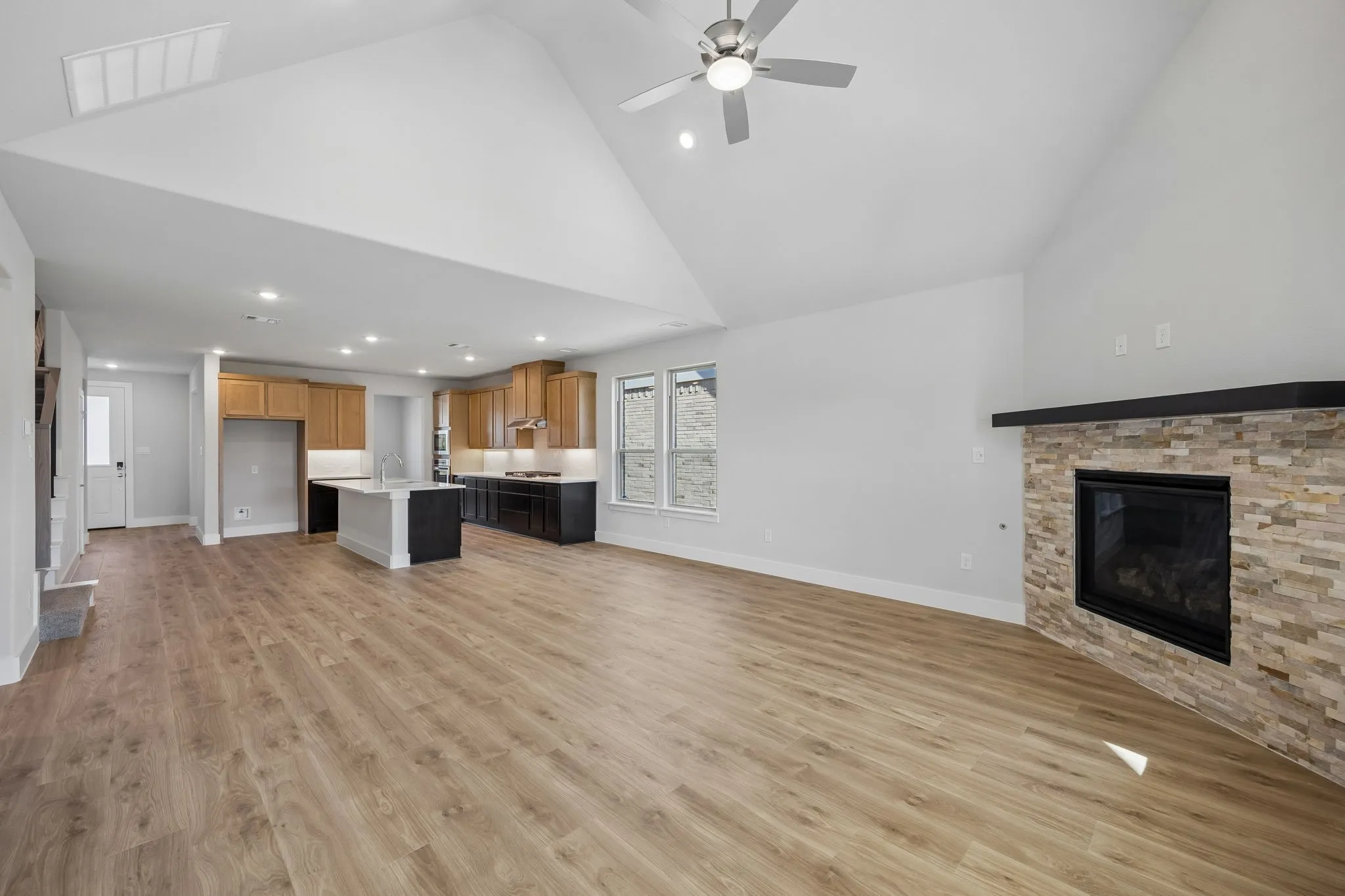 Open-concept living space featuring wood-finish flooring, a vaulted ceiling, and a stacked stone fireplace with a dark mantel