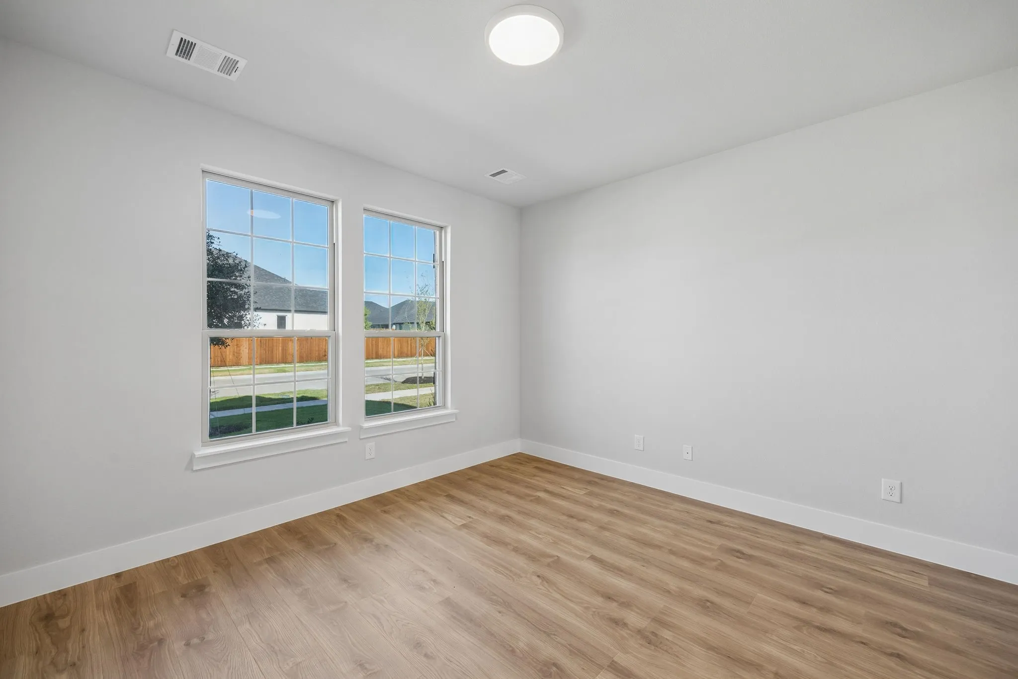 Bright interior space featuring two large windows, wood-finish flooring, and a flush-mount ceiling light
