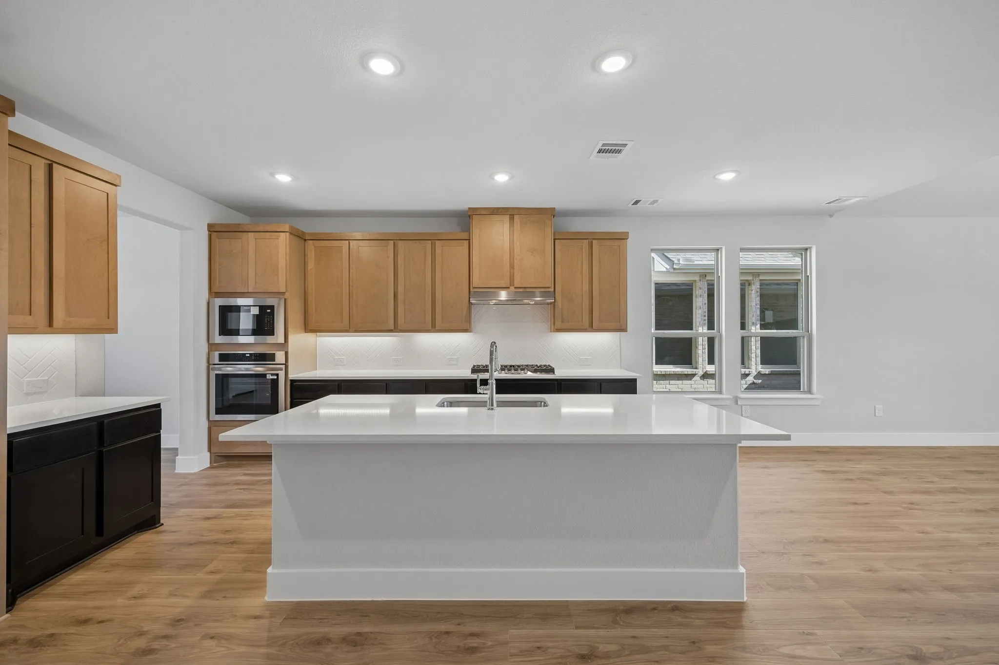 Kitchen featuring a large island, wood-finish flooring, two-tone cabinetry, stainless steel appliances, and recessed lighting