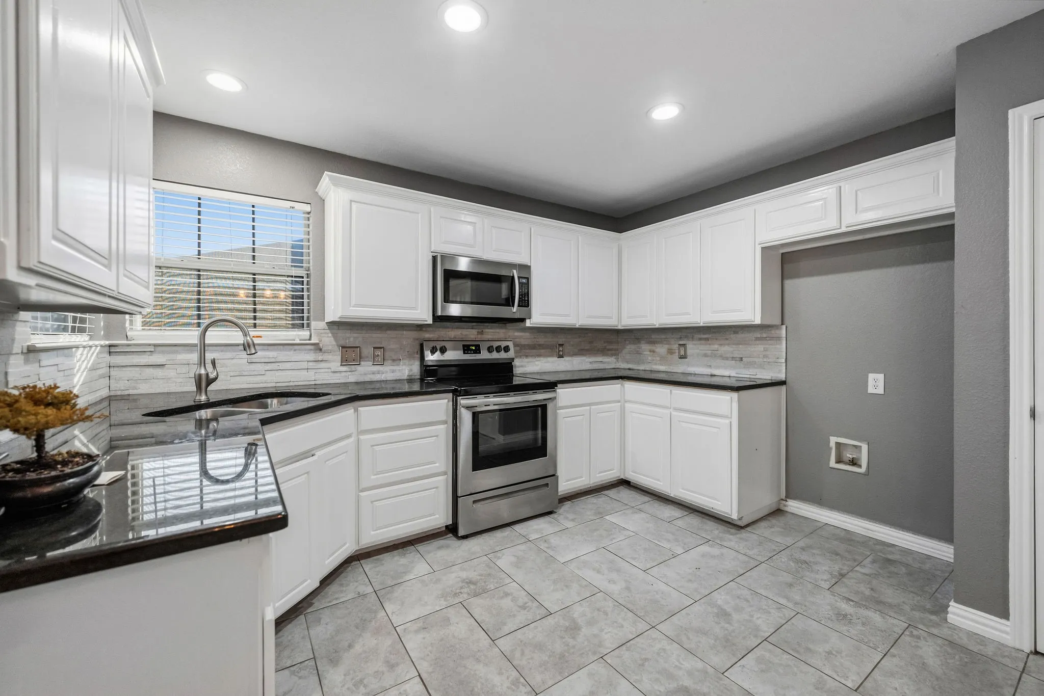 White cabinetry, stainless steel appliances, black countertops, tile flooring, and a tiled backsplash