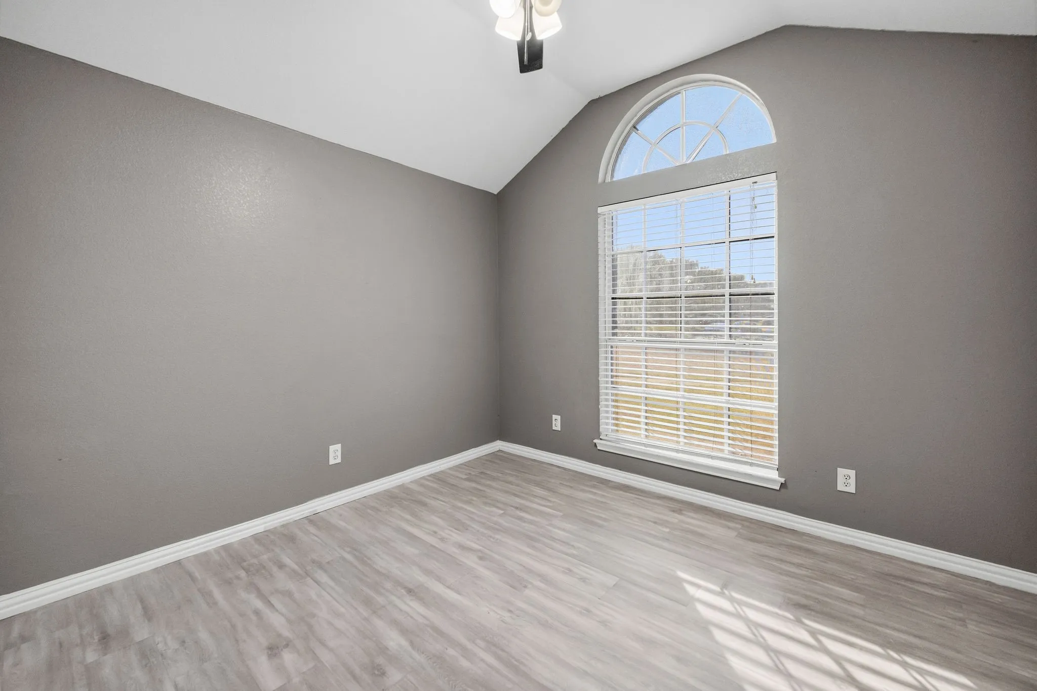 Vaulted ceiling with a ceiling fan, arched transom window, large rectangular window with blinds, and wood-finish flooring