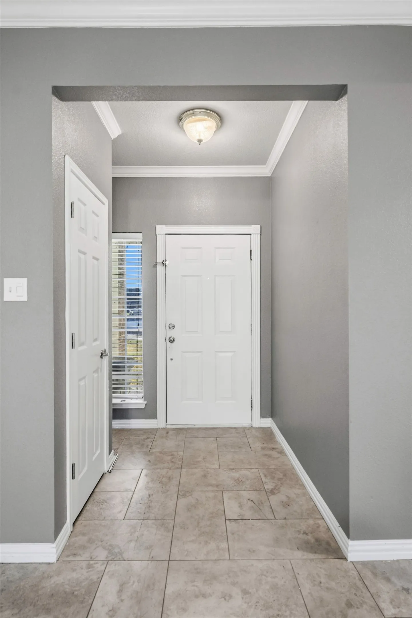 Foyer with neutral-toned tile flooring, white crown molding, and a flush mount ceiling light fixture