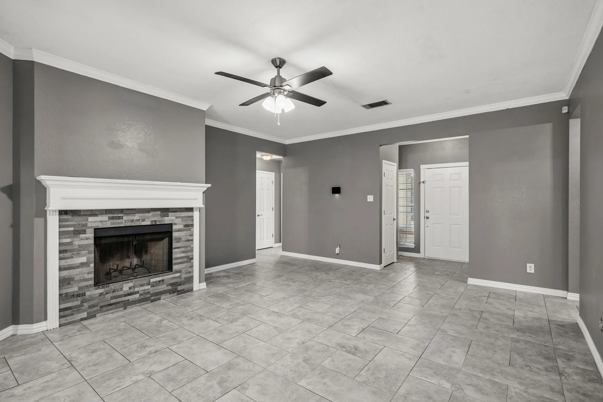 Spacious room featuring tile flooring, a fireplace with a stone surround and white mantel, a ceiling fan, and crown molding