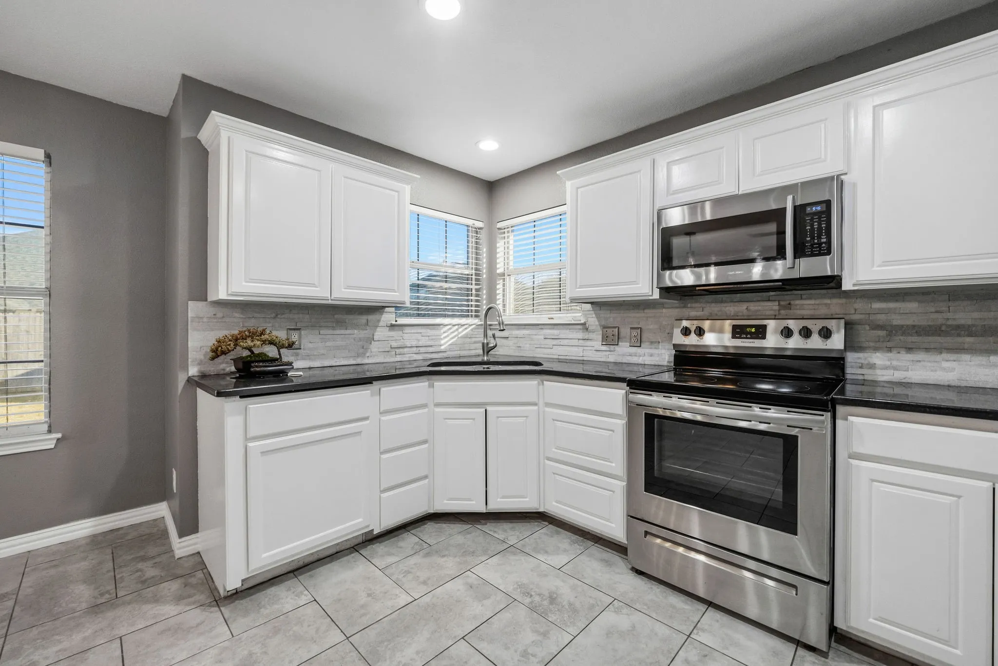 Kitchen featuring white shaker cabinetry, dark countertops, a tiled backsplash, stainless steel appliances, and tiled flooring