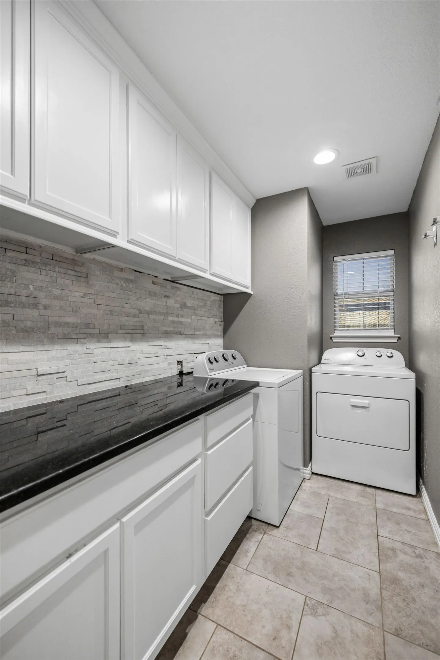 White cabinetry with black countertop, stone tile backsplash, and tile flooring